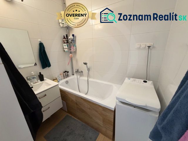 Bathroom in a 3-room apartment with a bathtub, sink, and washing machine, white tiles.