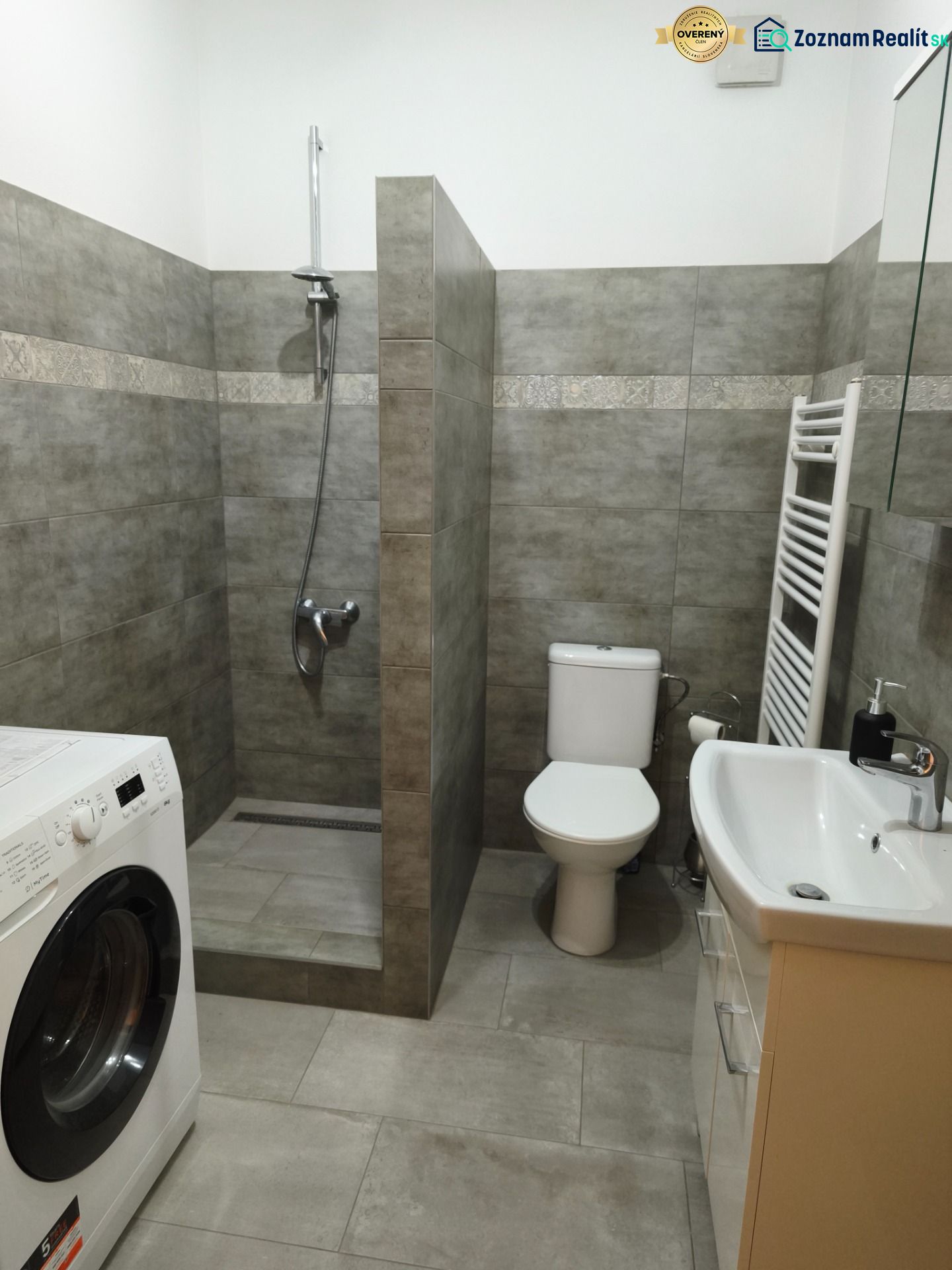 Bathroom in a studio apartment with a washing machine, shower, and toilet.