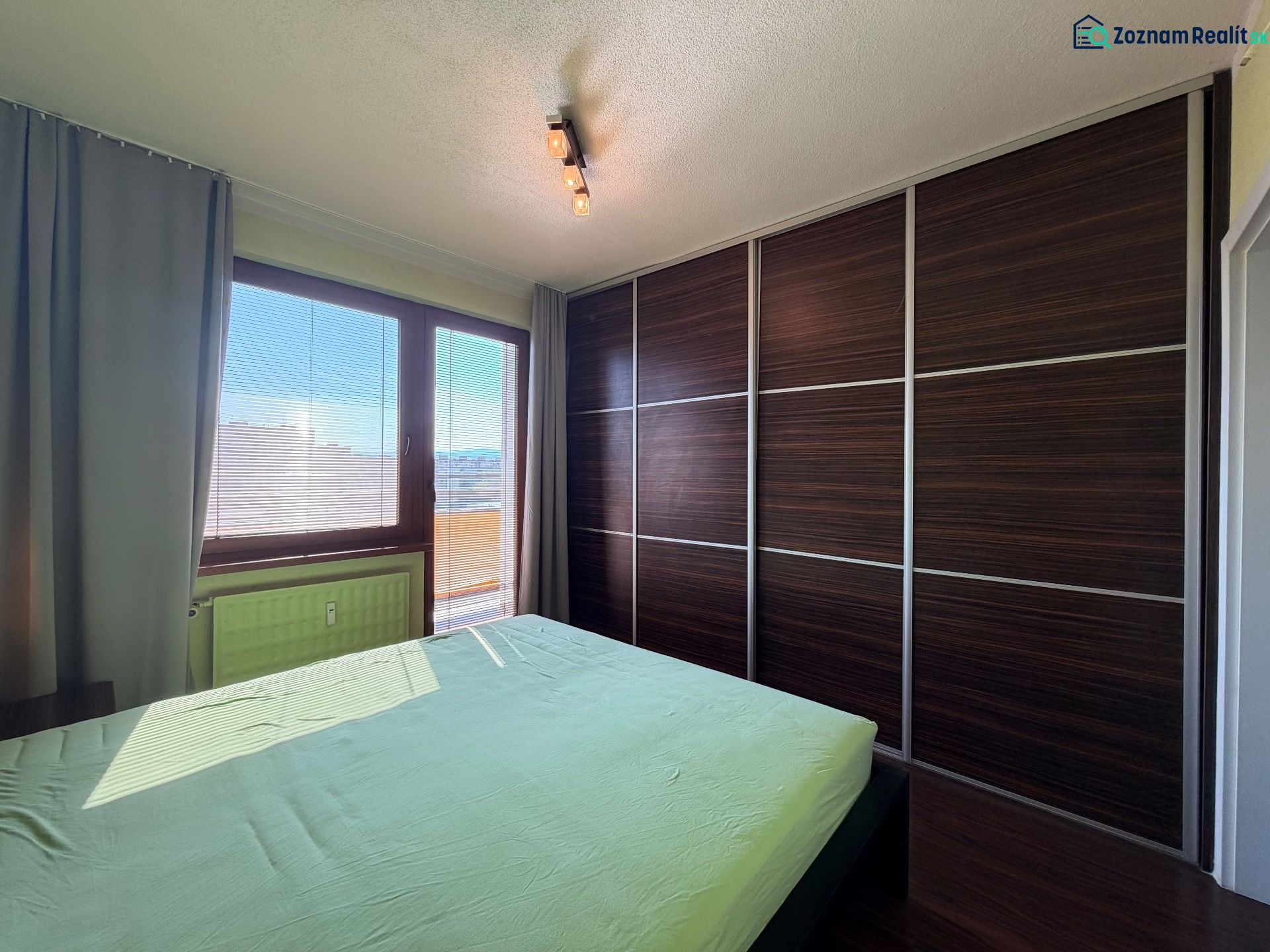 A bedroom in a three-room apartment with a wood-patterned floor and a large built-in wardrobe.