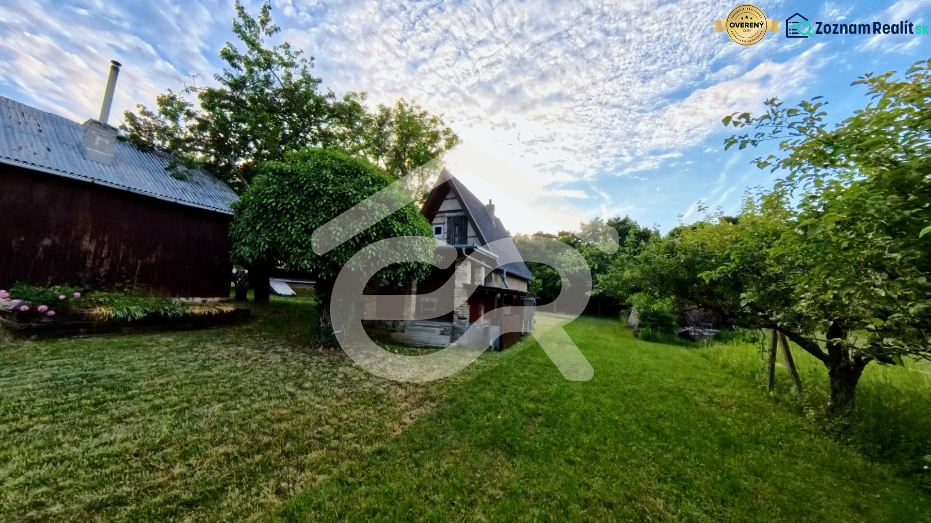 A cottage in Podhorany surrounded by greenery, with a blue sky and clouds in the background.