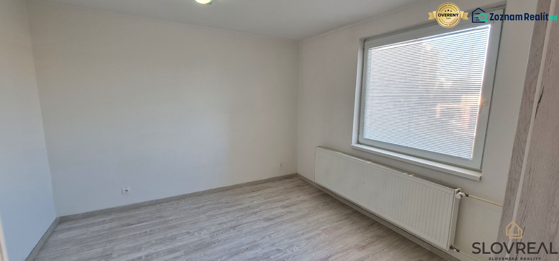 A room in a 2-room apartment with white walls and a wooden decor floor.