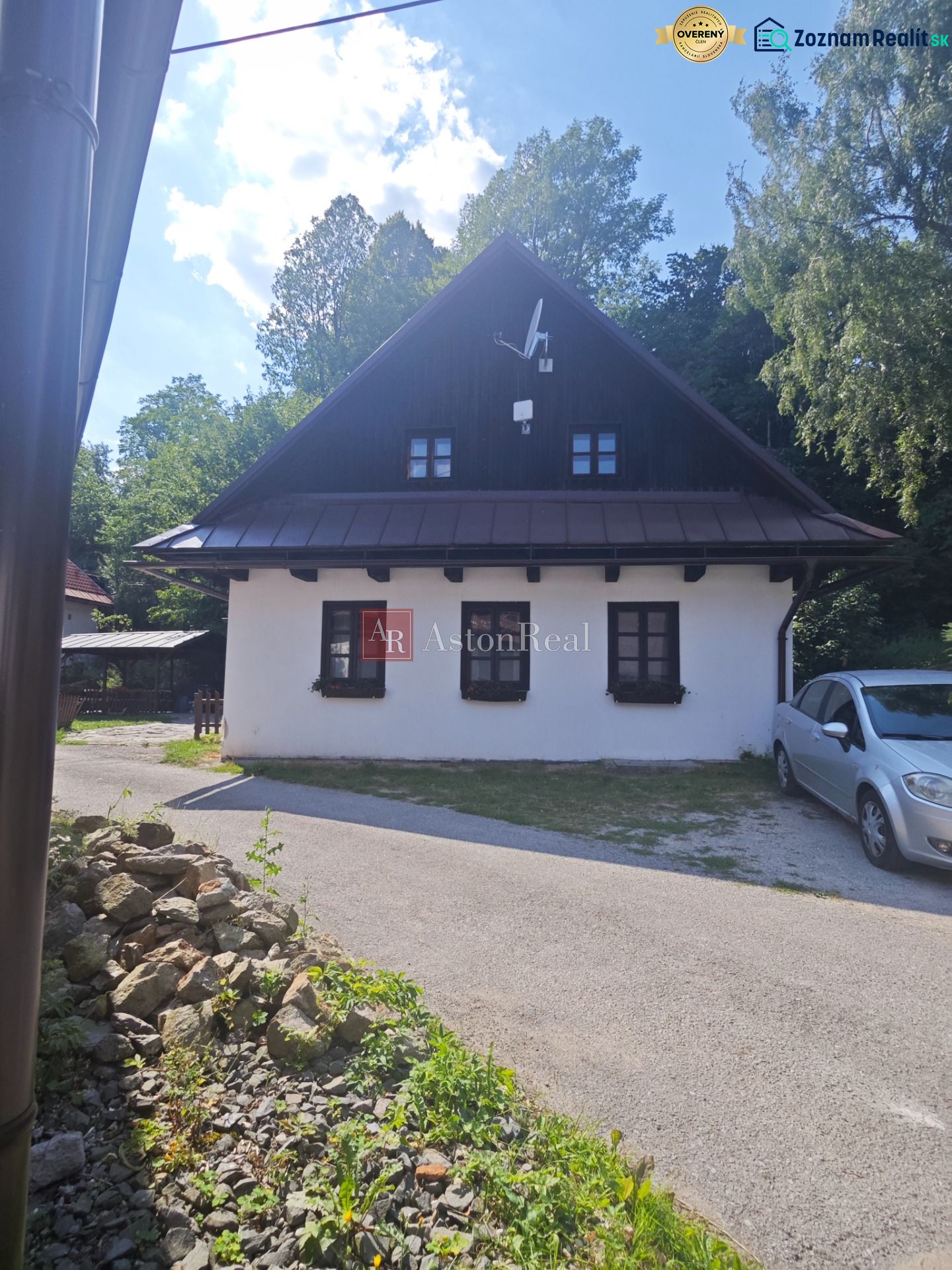 A cottage in Špania Dolina with a white facade and a satellite dish, surrounded by greenery.