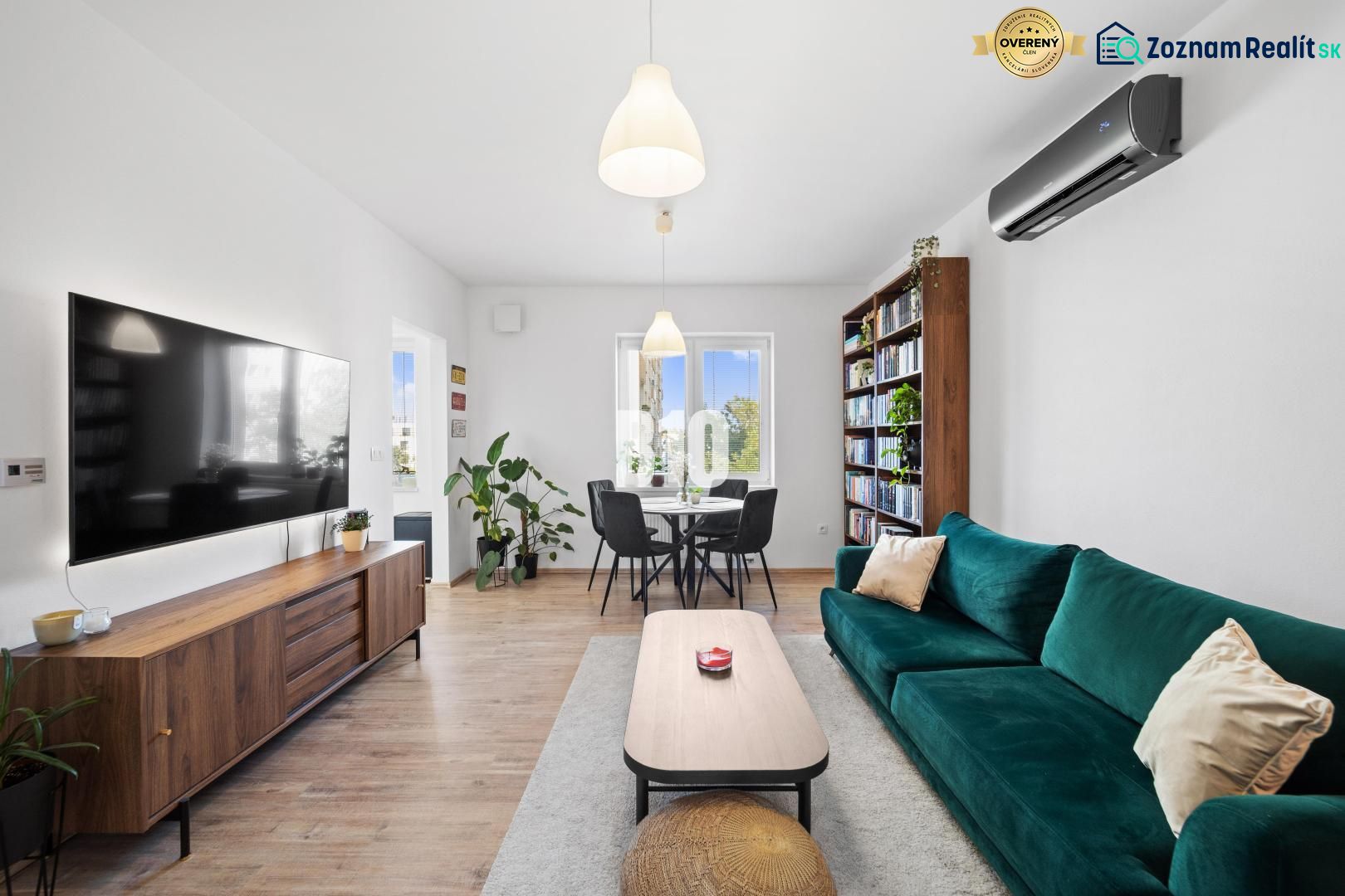 Living room in a two-room apartment with a large television, a bookshelf, and a wooden decor floor.