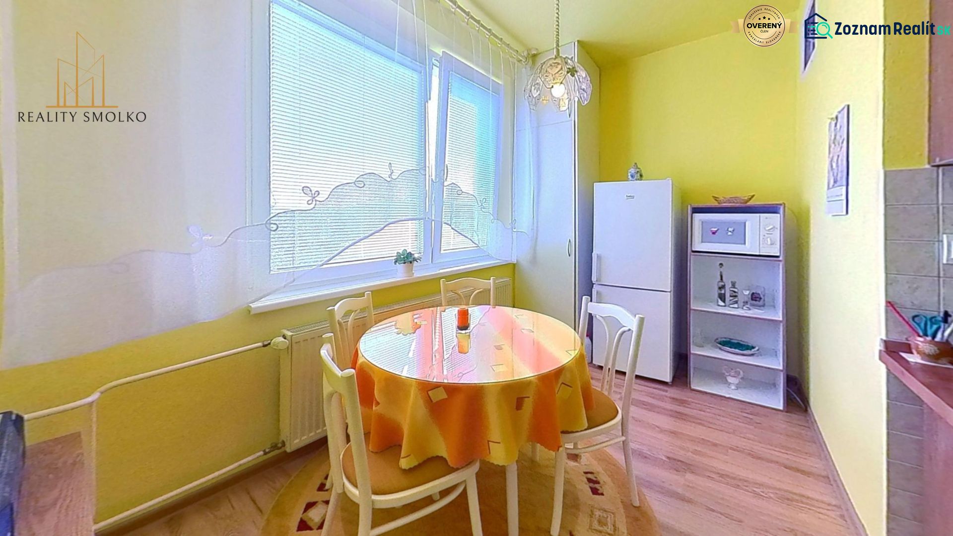 Yellow kitchen with a dining table, refrigerator, and shelf in a two-room apartment.