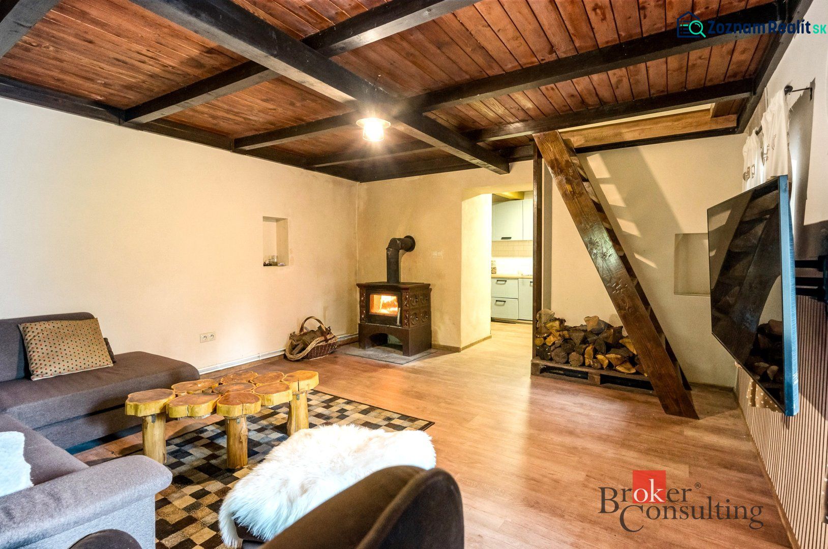 The interior of a cottage with a wooden beam ceiling, a stove, and a floor with a wooden decor.