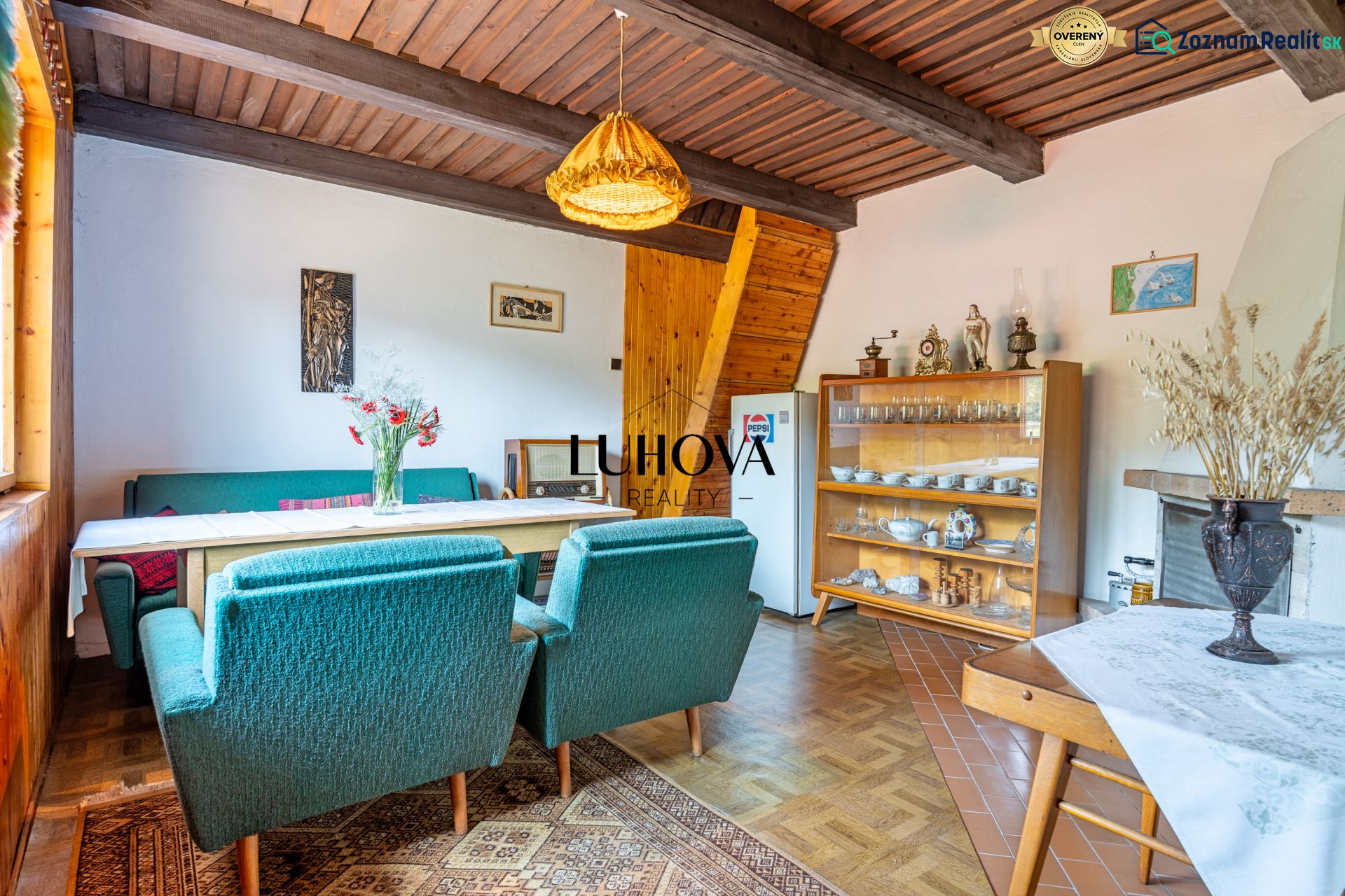 The interior of a cabin with green armchairs, a dining table, and a cabinet with dishes.
