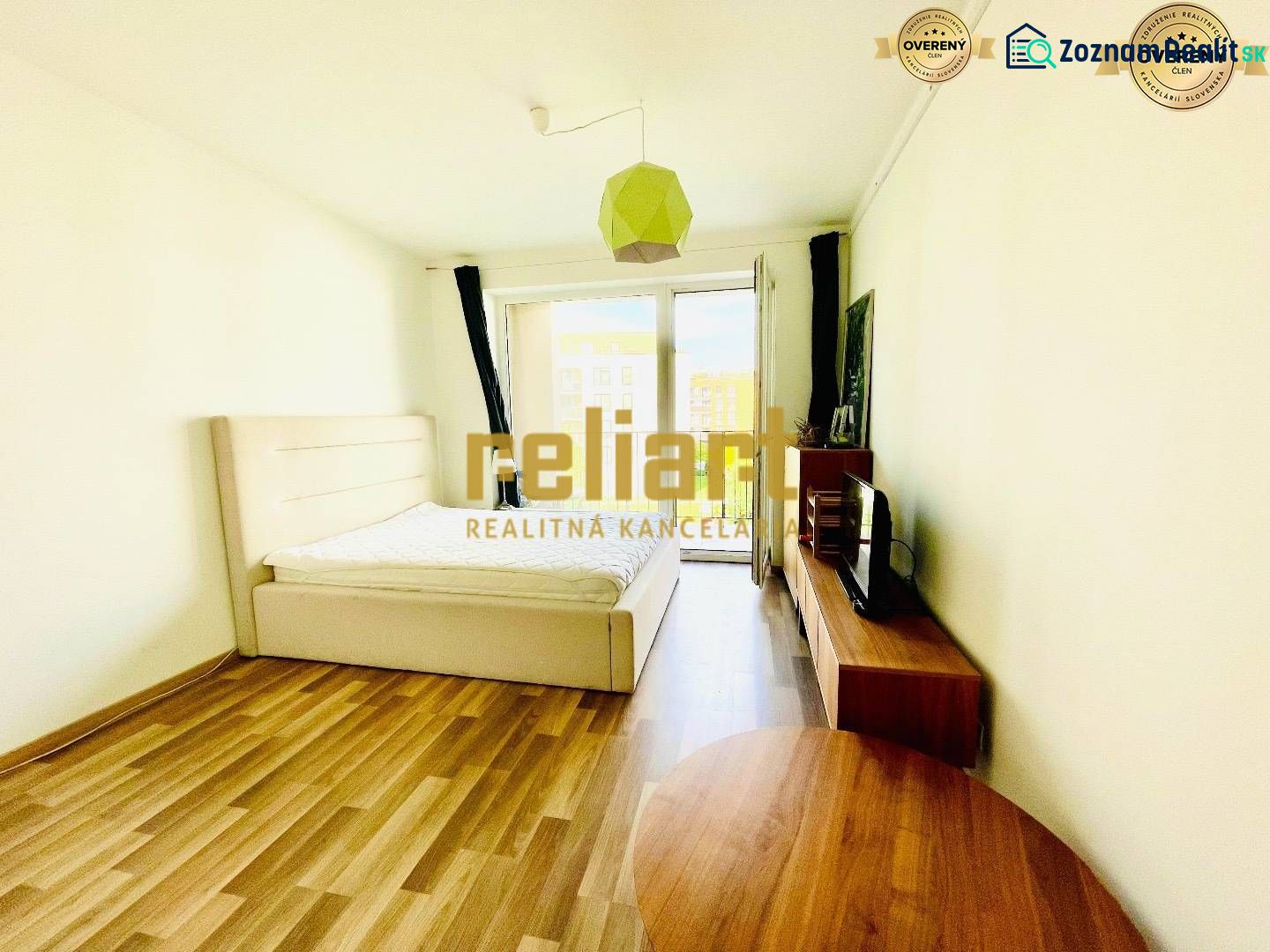 Interior of a 1-room apartment with a bed, television, and wooden decor flooring.