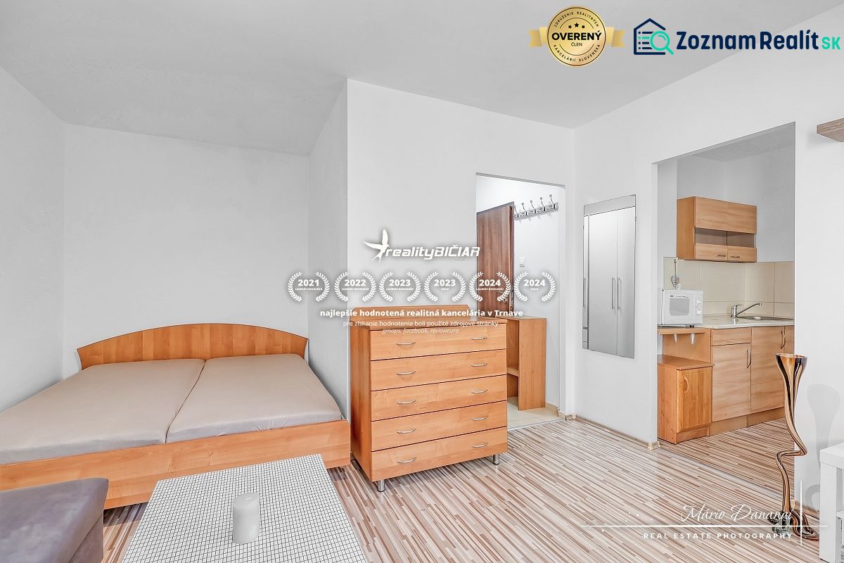 A studio apartment with a bed, a dresser, and a kitchenette with a wooden decor floor.