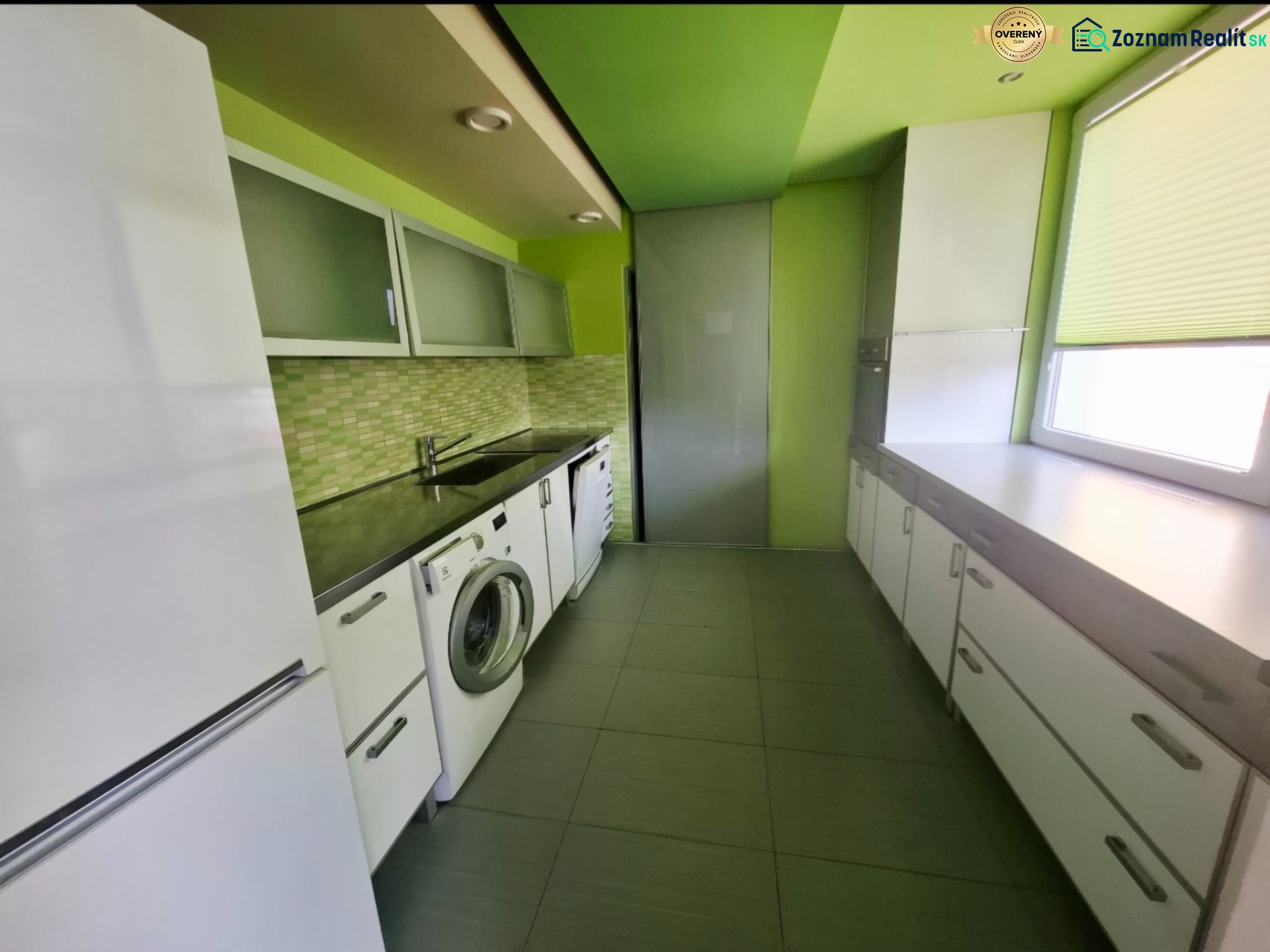 A kitchen in a 3-room apartment with a washing machine, white furniture, and green walls.