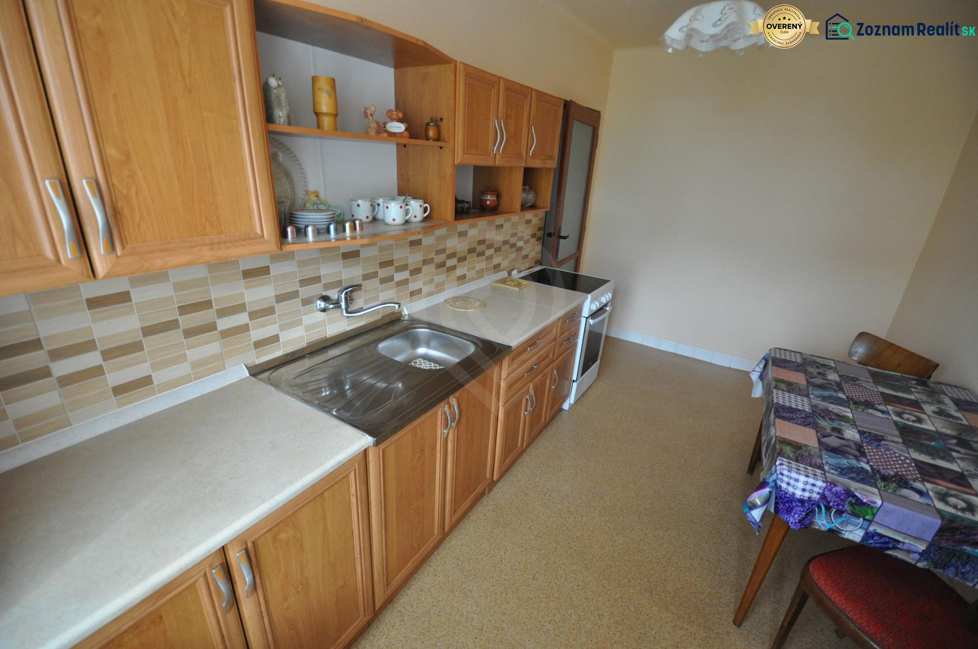 A kitchen in a 2-room apartment with wooden cabinets and tiled backsplash.
