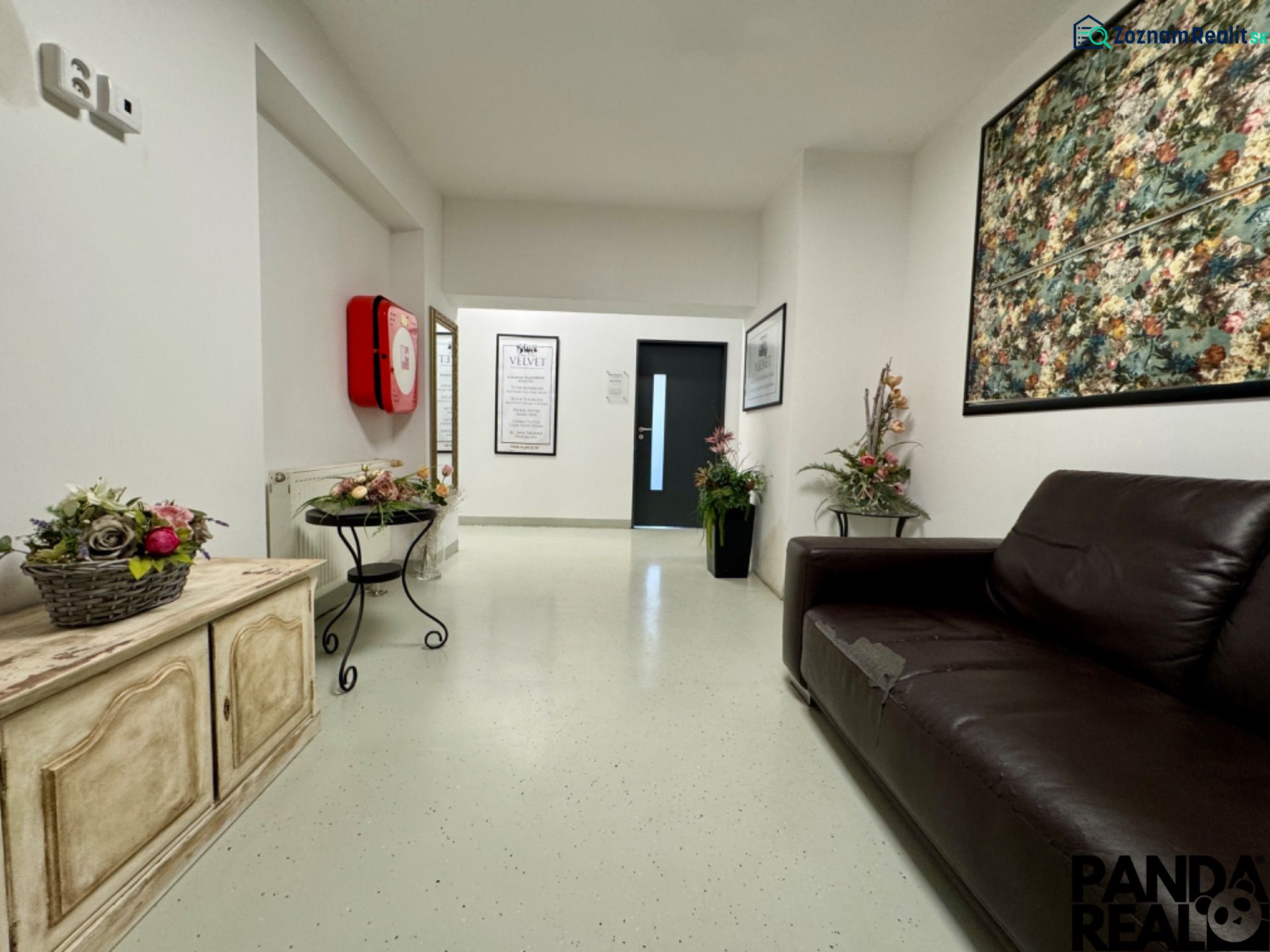 Reception in commercial premises with a dark sofa and floral decorations.