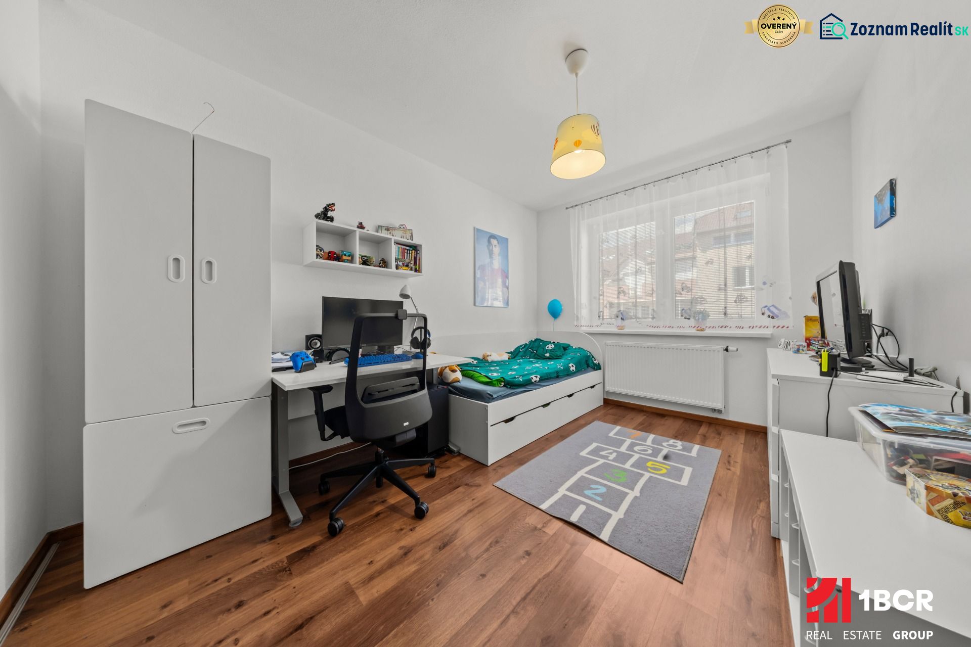 Children's room with a wooden decor floor in a 2-room apartment, a computer desk, and a bed.
