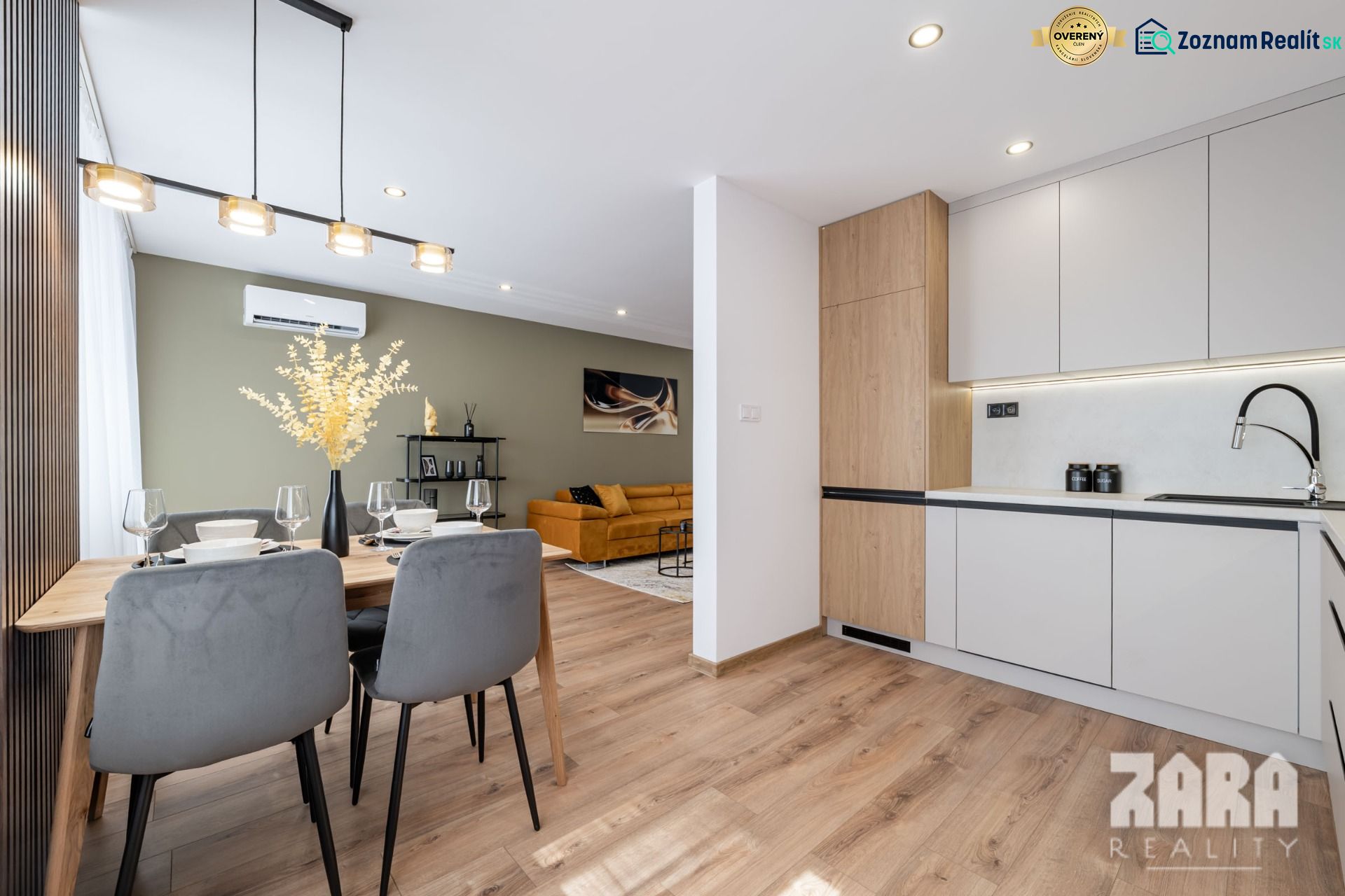 Dining room of a 3-room apartment with a decorative light fixture, flooring, and a sofa in the background.
