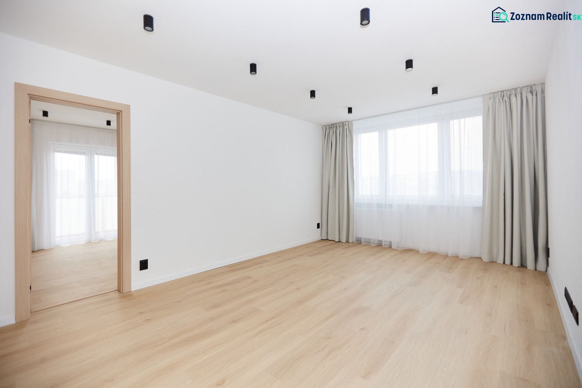 A spacious room in a 3-room apartment with a wooden decor floor and curtains.