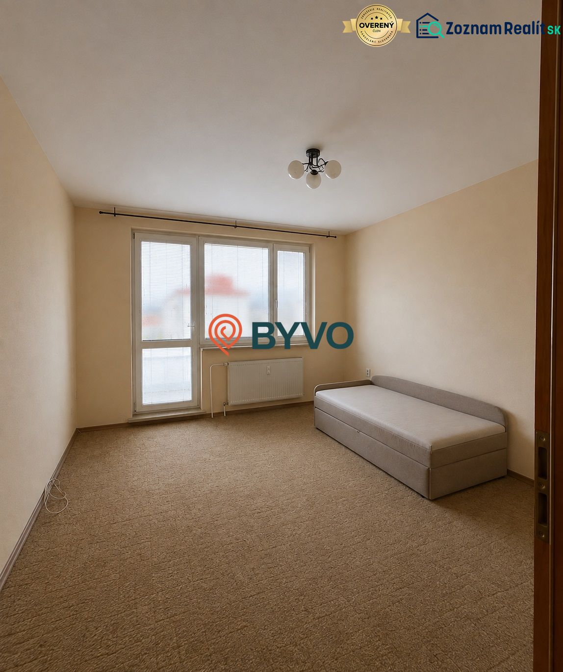 A room in a 3-room apartment with a carpet and a simple bed, bright walls.