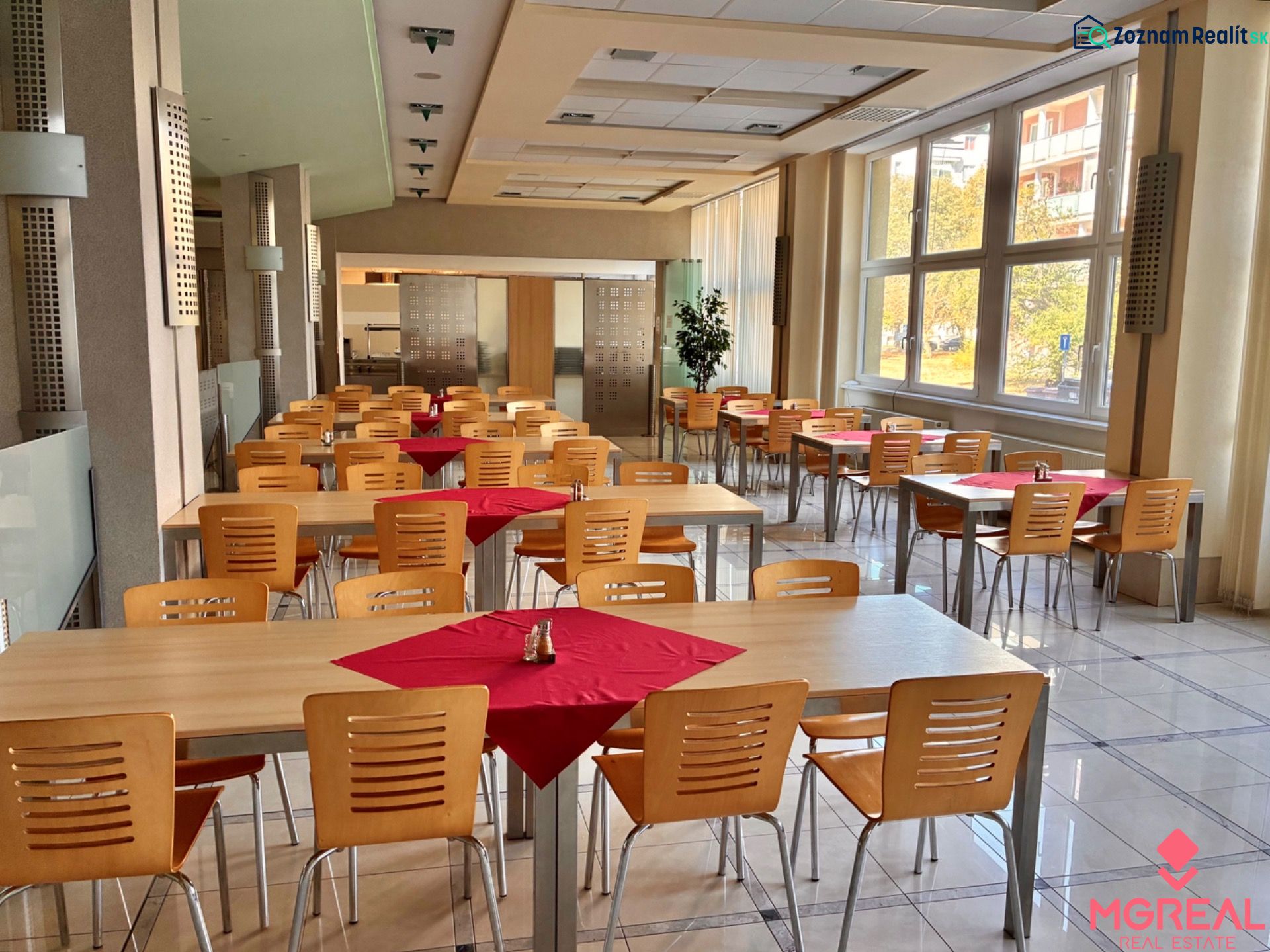 A bright office canteen with wooden tables, chairs, and large windows.