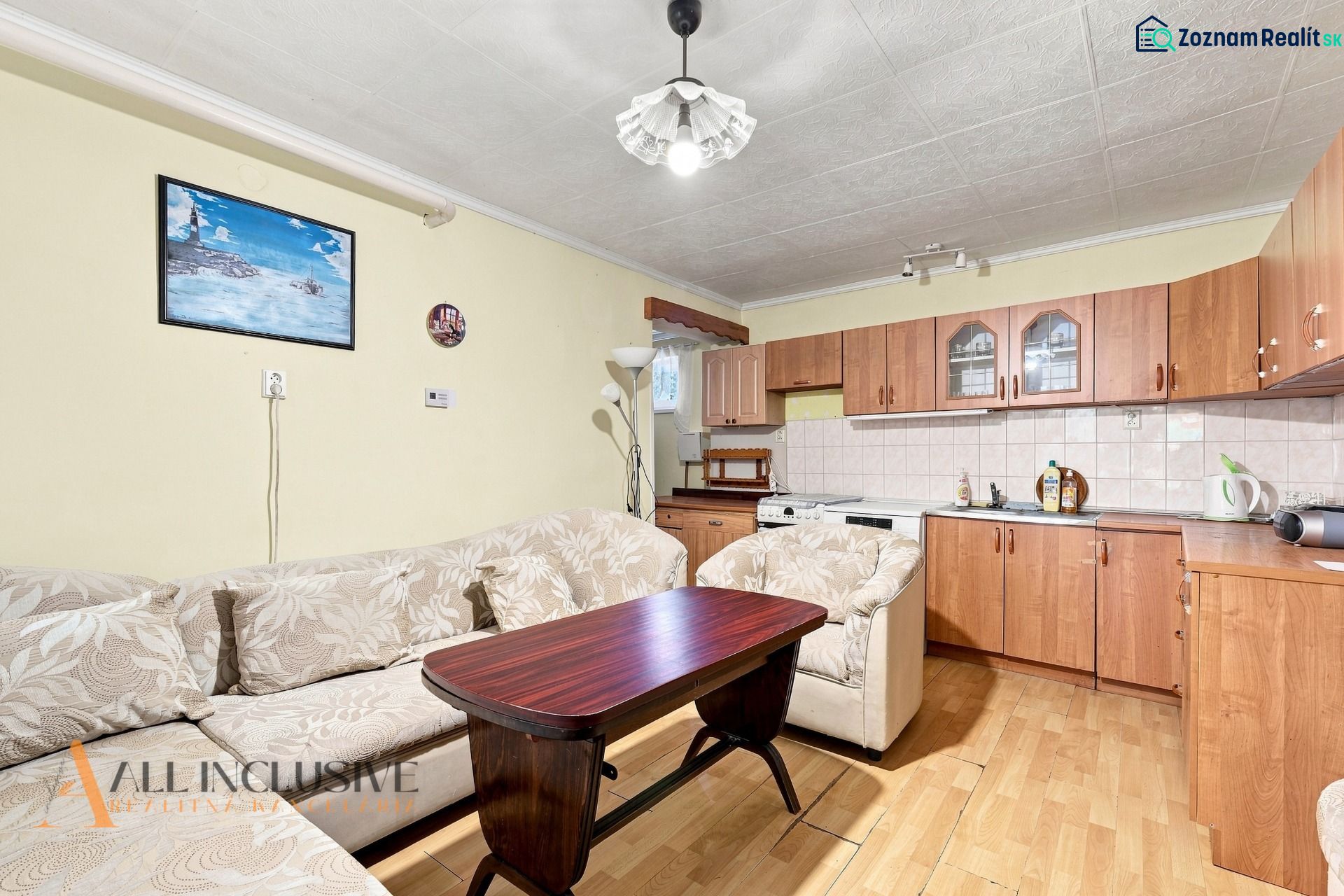 Living room with a kitchenette, sofa, and wooden decor flooring in a family house.