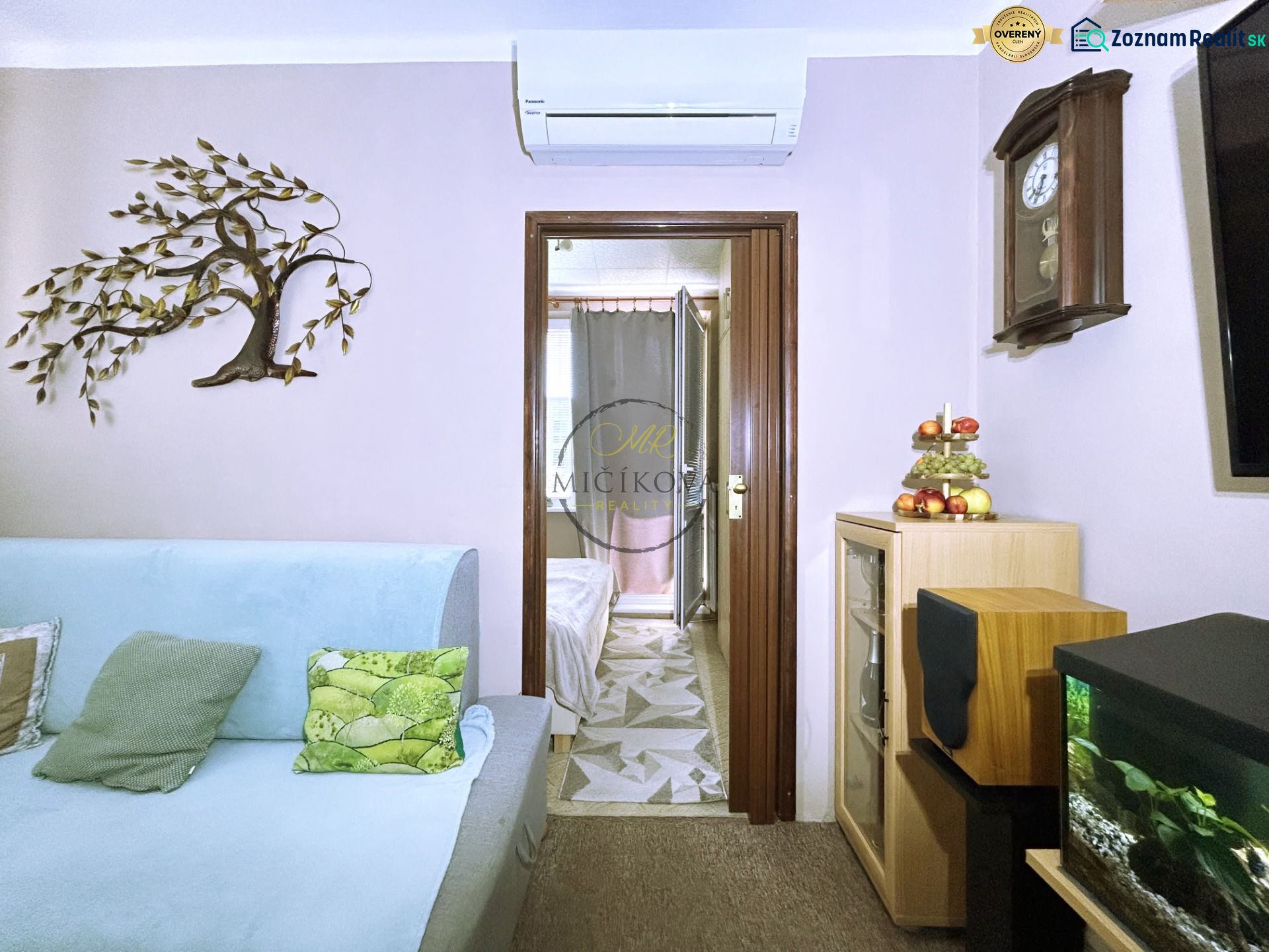 A tree decoration on the wall next to a light blue sofa, an aquarium, and antique clocks.