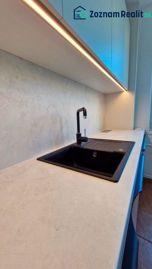 A kitchen in a 3-room apartment with a white countertop and a black sink.