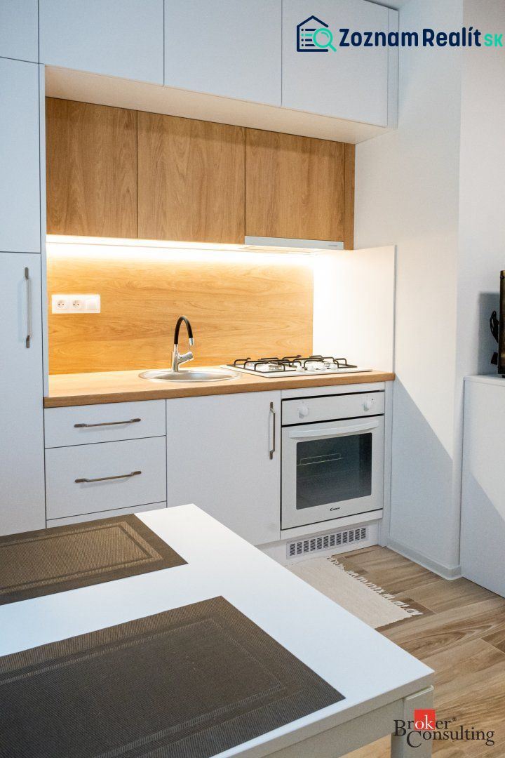 A kitchenette in a studio apartment with a wooden decor floor and comfortable lighting.