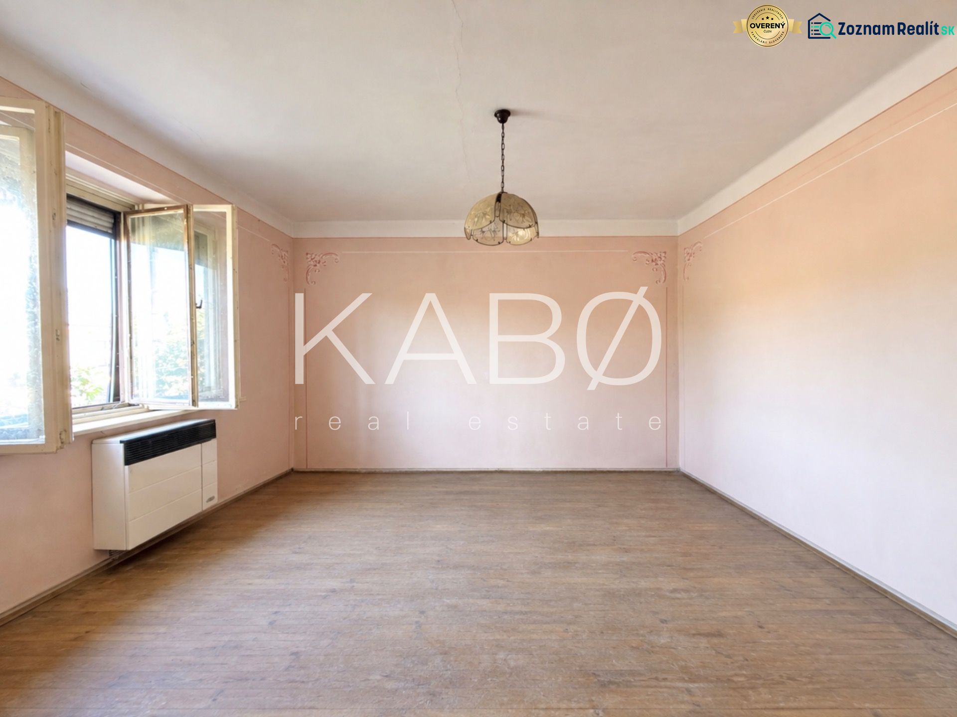 Empty room with wood-patterned flooring, pink walls, and a hanging light fixture.