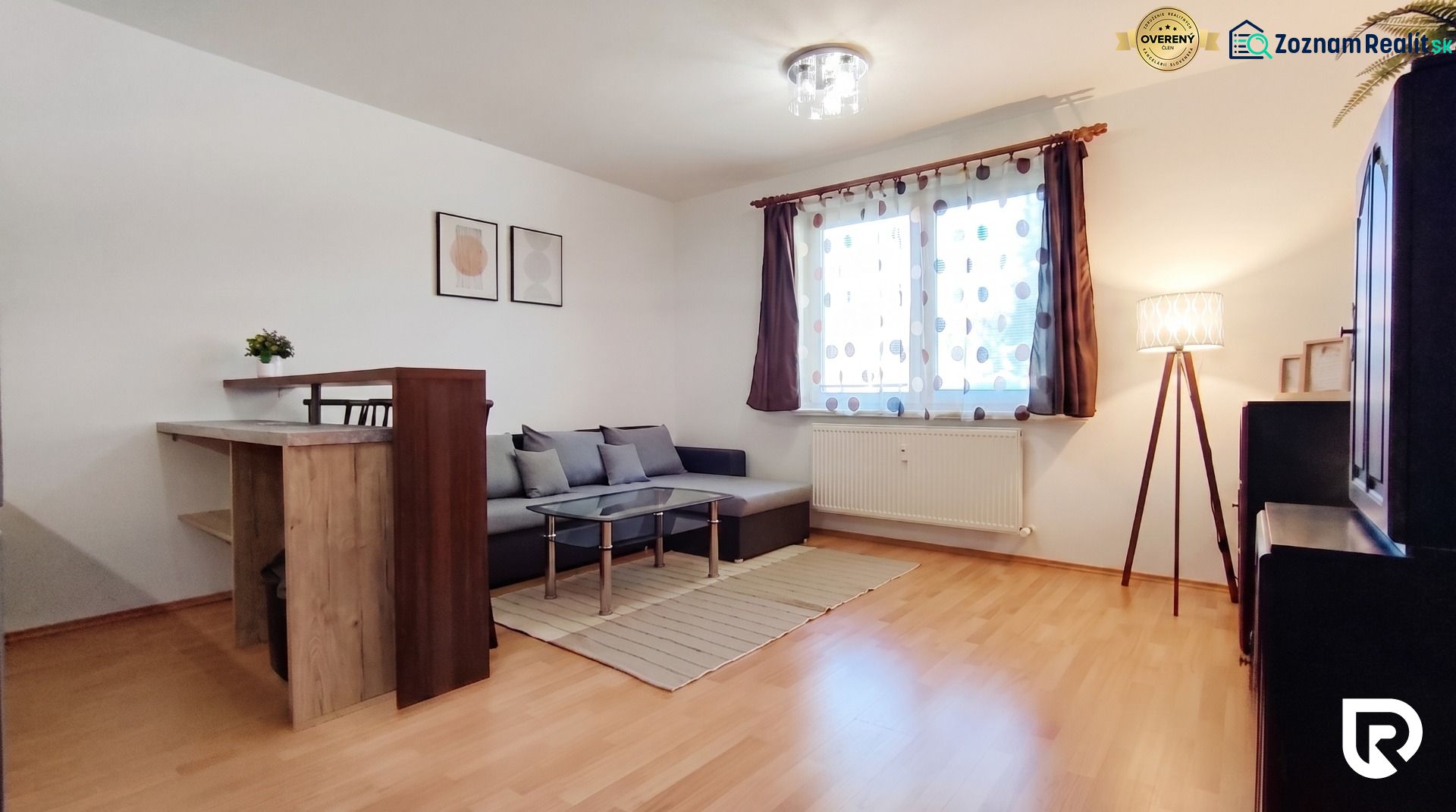 Living room in a two-room apartment with a wooden decor floor, gray sofa, and table.