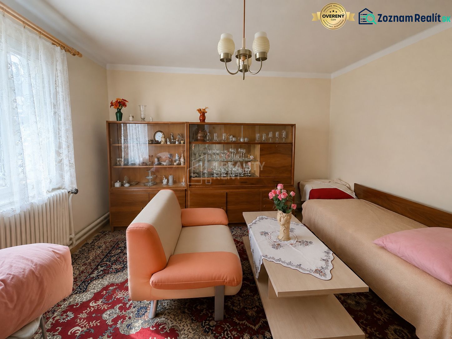 A room in a family house with a sofa, a display cabinet, and a carpet with a floral pattern.