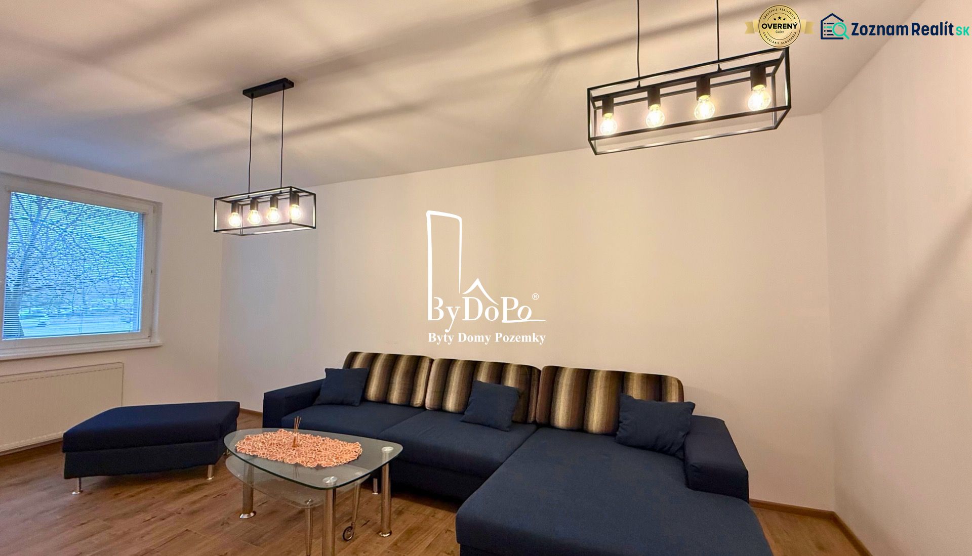 Living room with a sofa, chandelier, and wooden decor flooring in a three-room apartment.