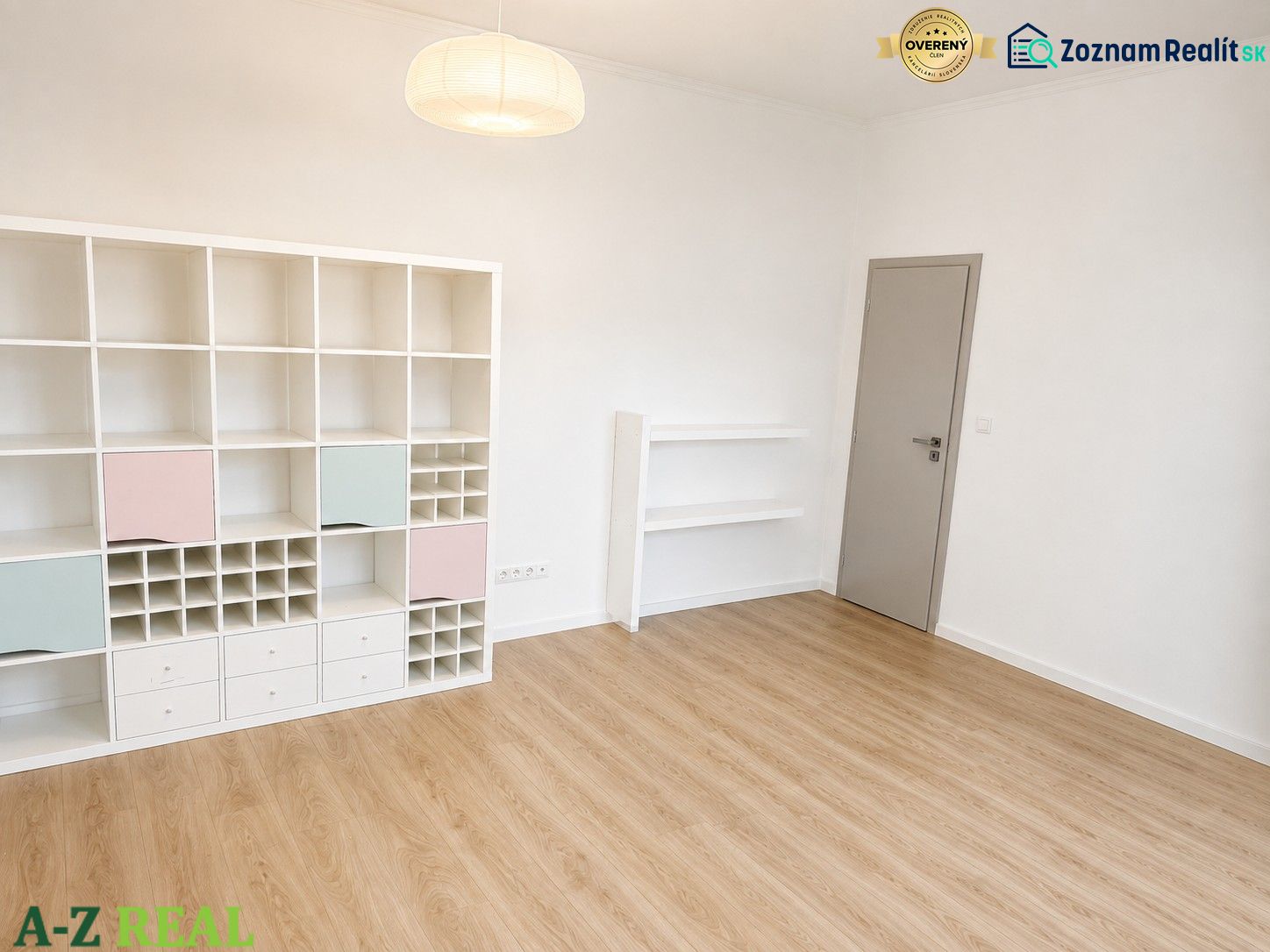 A room in a 3-room apartment with a wooden decor floor and a white shelf.