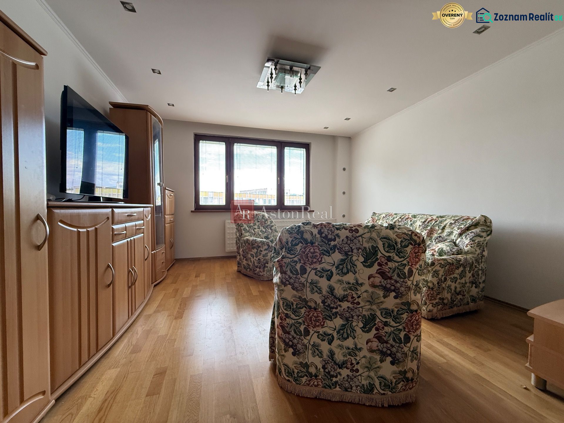 Living room in a 4-room apartment with a floral sofa and wooden decor flooring.