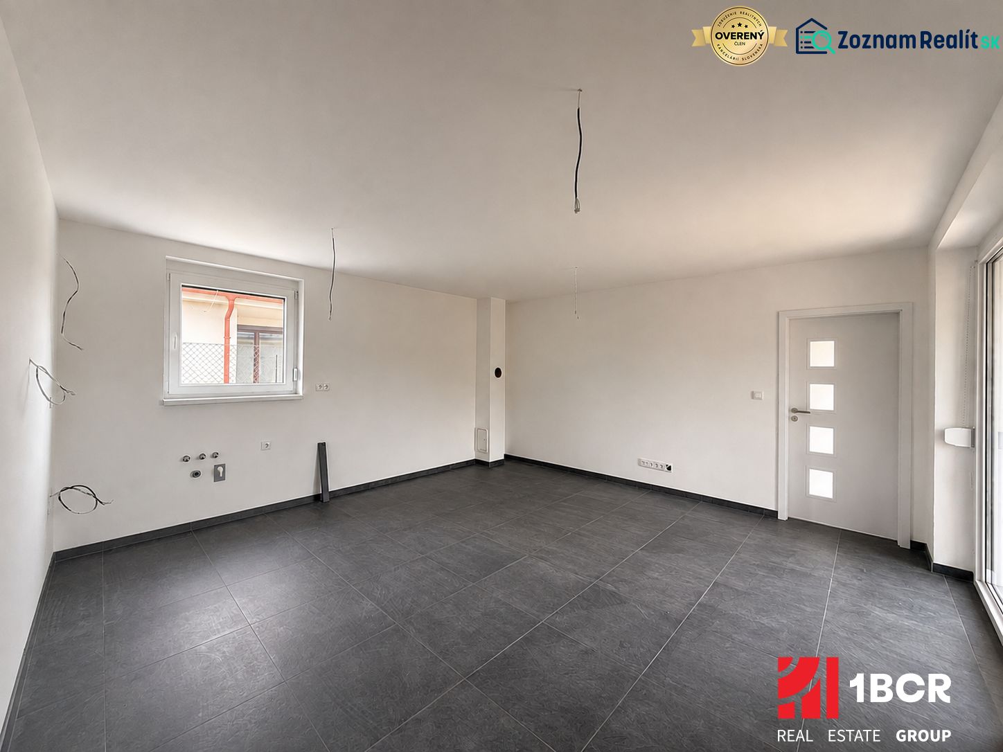 A bright room with dark ceramic tiles and a large window in a family house.