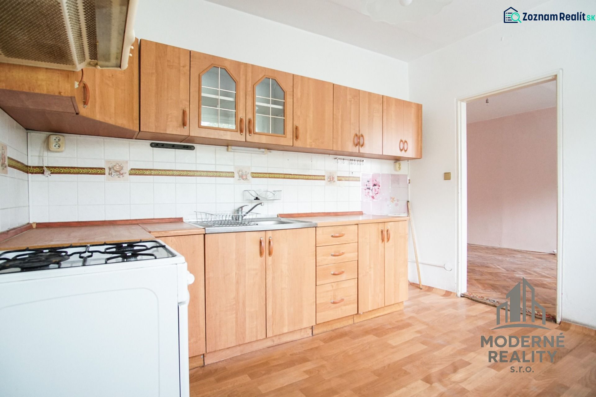 A kitchen in a 3-room apartment with a light-colored kitchen unit and a floor with a wood design.