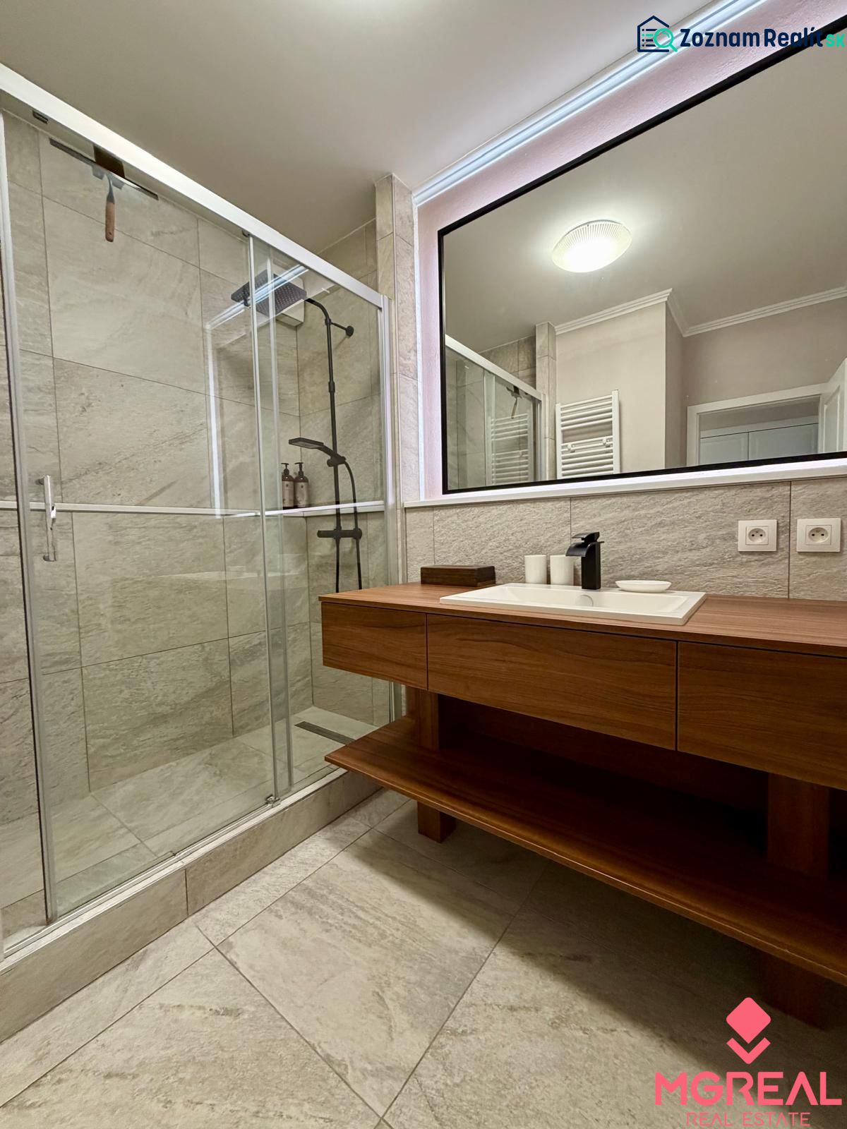 The bathroom of a two-room apartment with a spacious shower and a sink on a wooden cabinet.