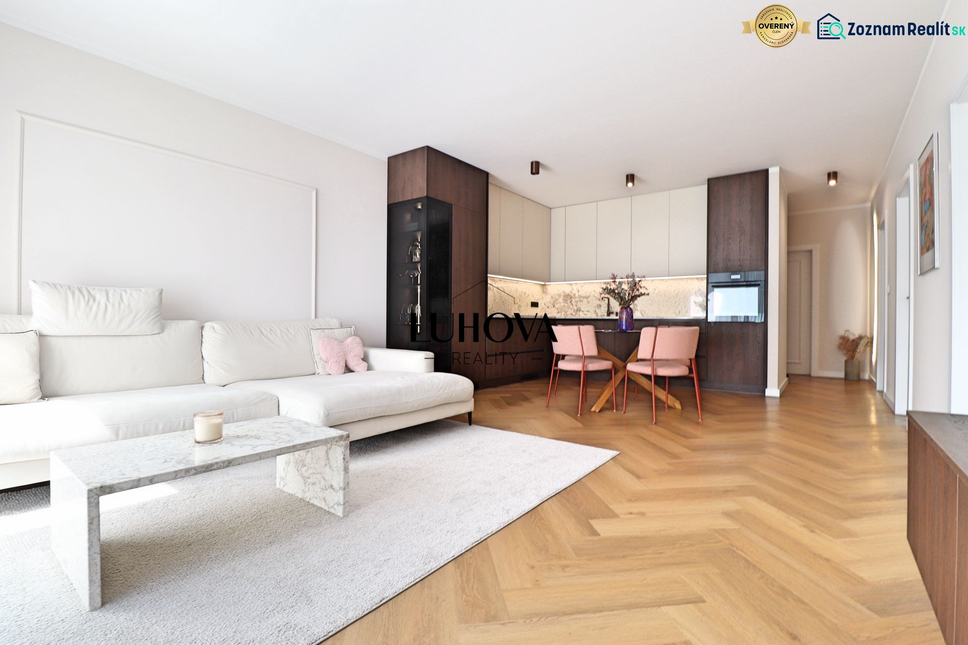 Living room with a white sofa, kitchenette, and wooden decor flooring.