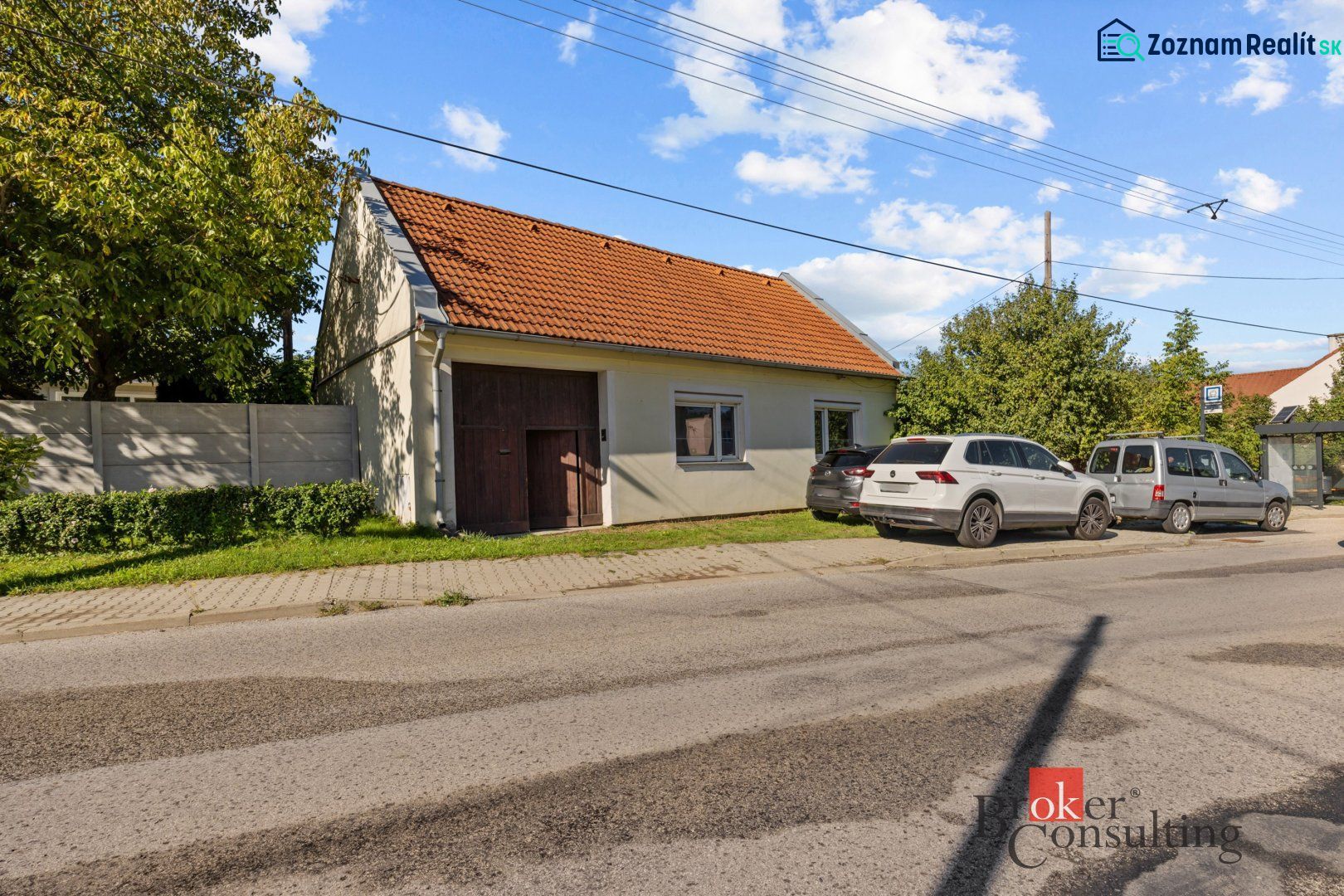 A family house in Budmerice with a red roof, cars parked in front of the house.