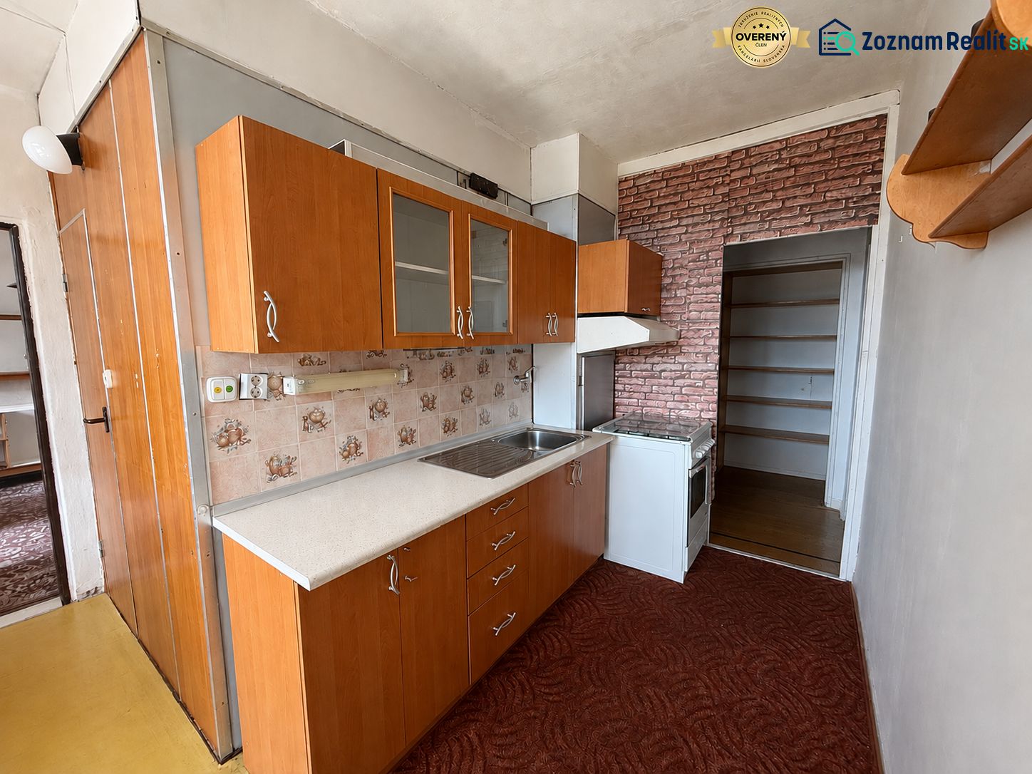 A kitchen in a 3-room apartment with tiles, a kitchen unit, and a brick-patterned wallpaper.