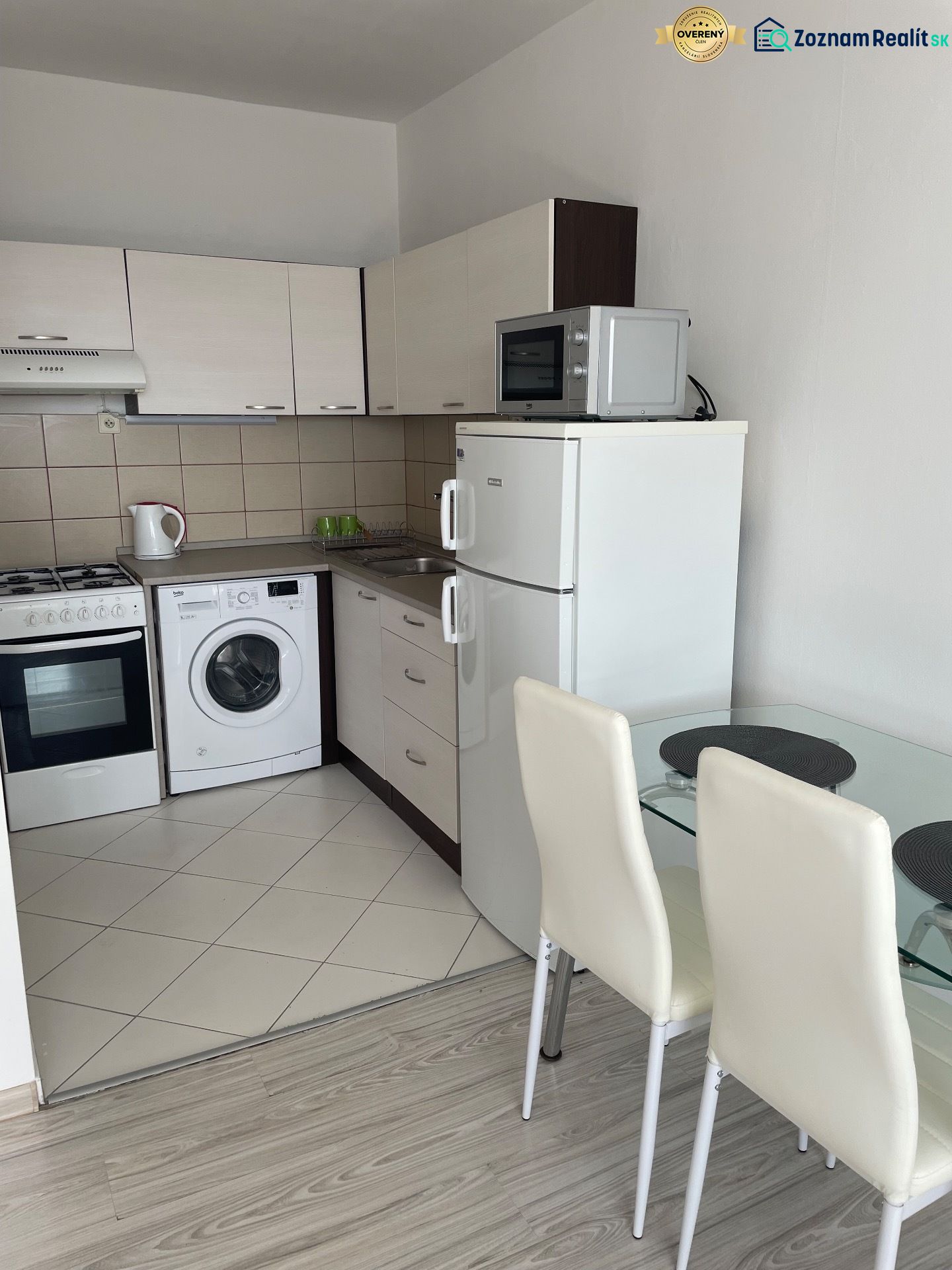 A kitchen in a studio apartment with a kitchenette, refrigerator, and wooden decor flooring.