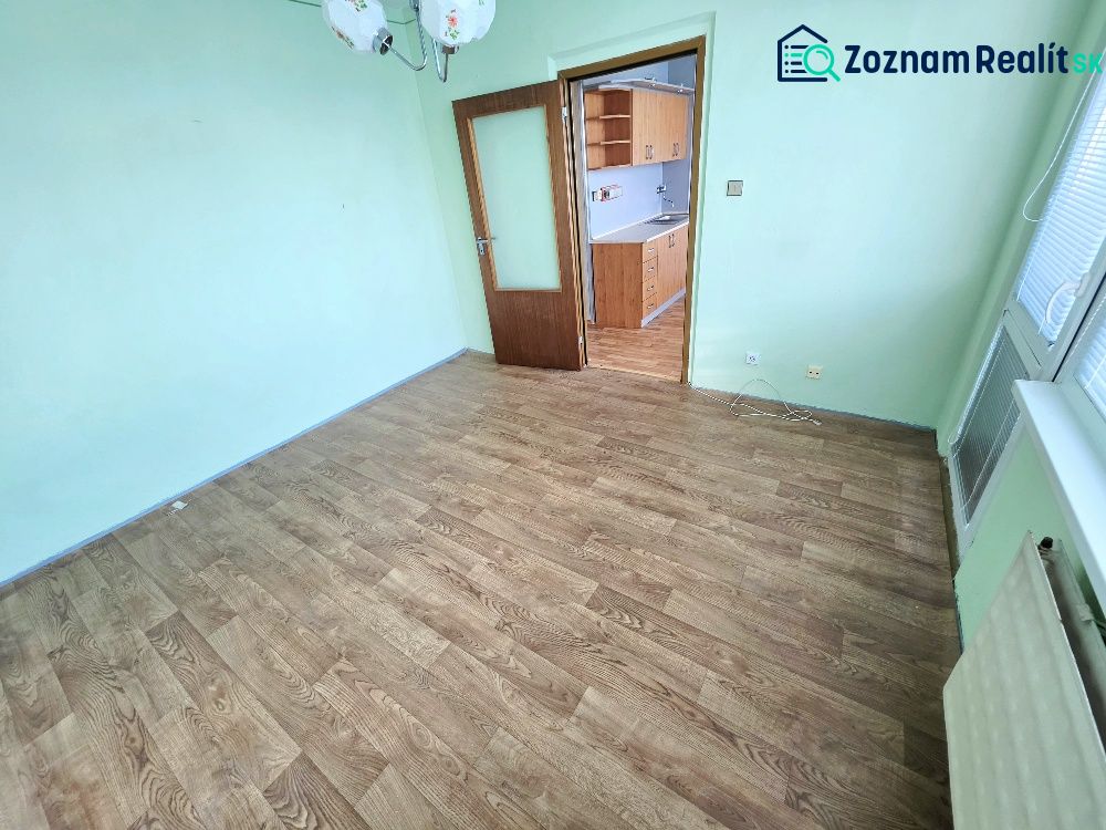 A room in a one-room apartment with a wooden decor floor and a transition to the kitchen.