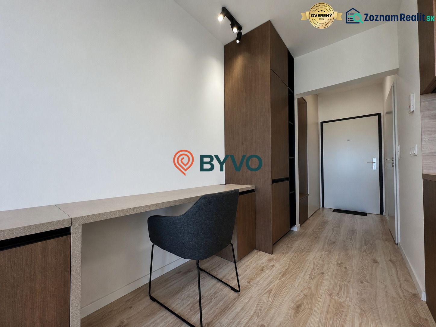 Studio apartment with a workspace, chair, and wood-patterned flooring, equipped with storage spaces.