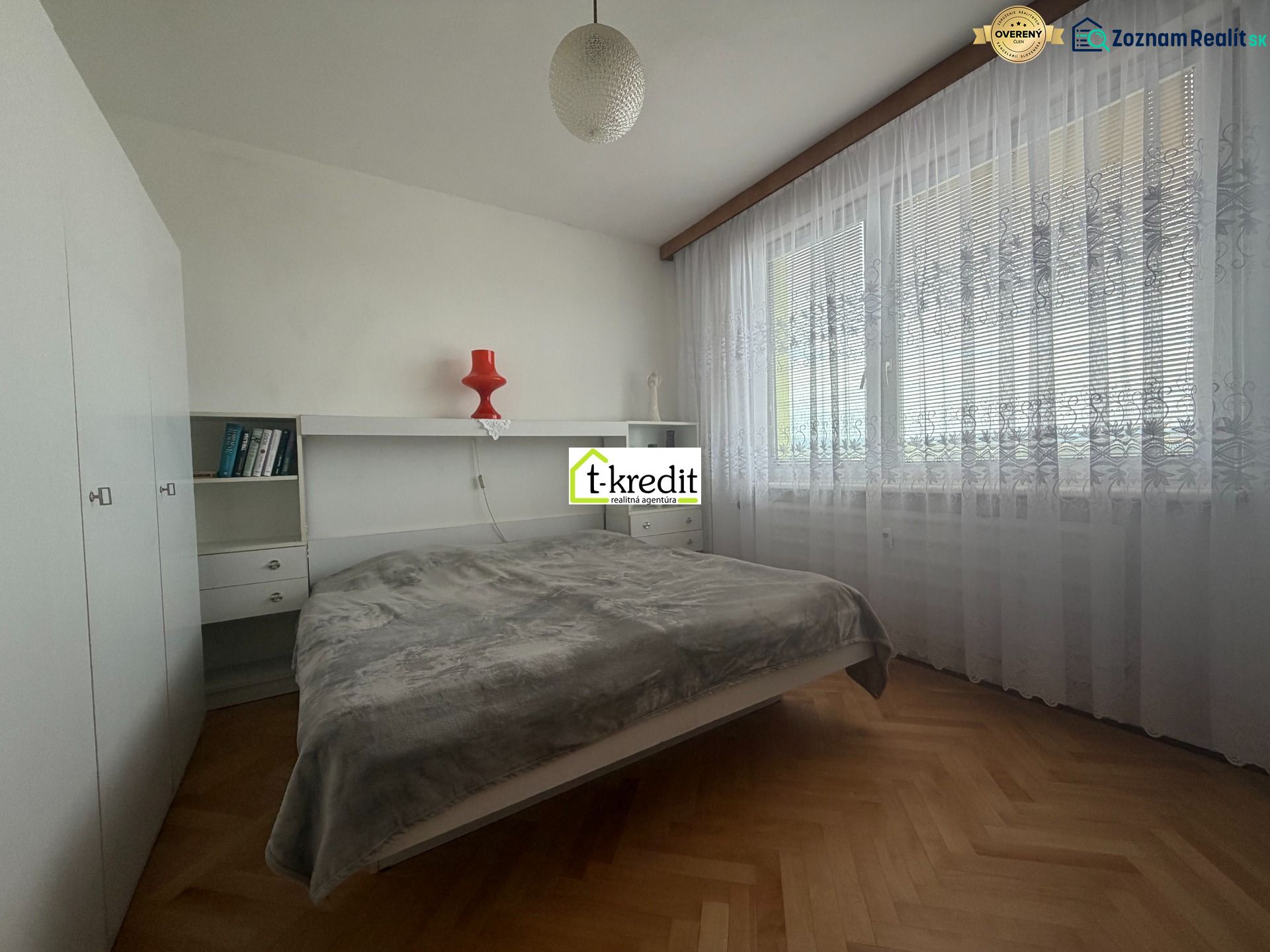 Bedroom in a 2-room apartment with wood-patterned flooring and large windows.