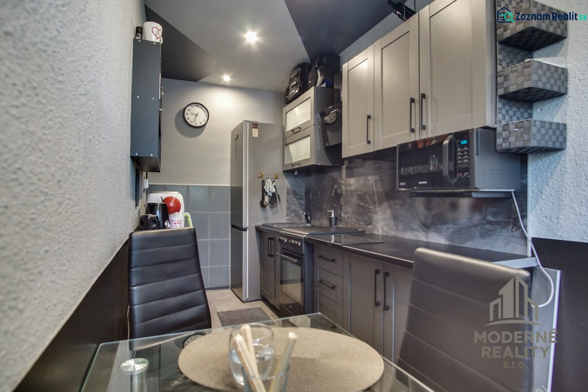 A kitchen in a 3-room apartment with dark gray kitchen cabinets and a dining table with a glass top.