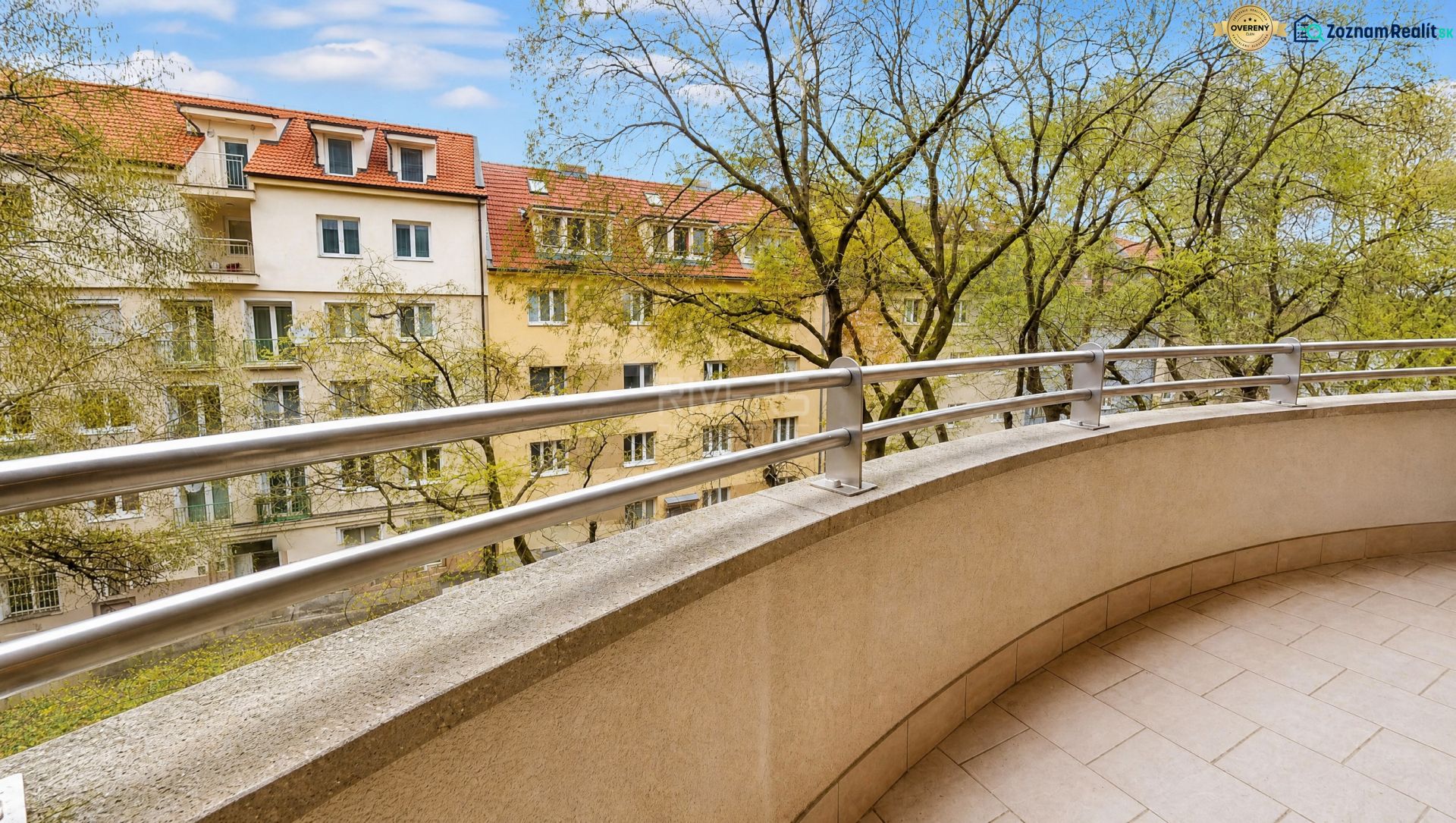 A balcony with a view of trees and apartment buildings on Kvačalova Street in Bratislava.