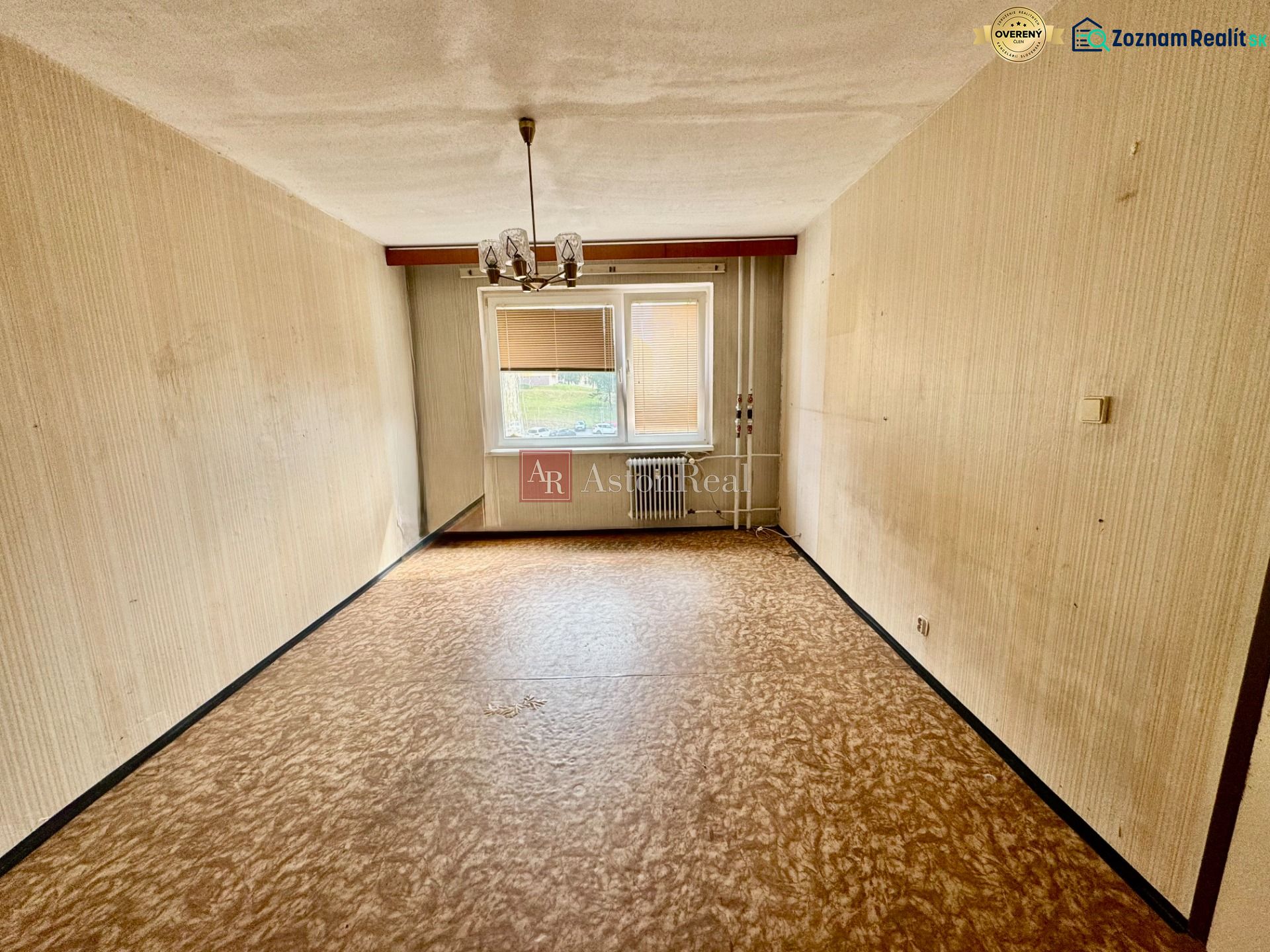 Living room in a two-room apartment, light walls, window with radiator, floor with wood decor.