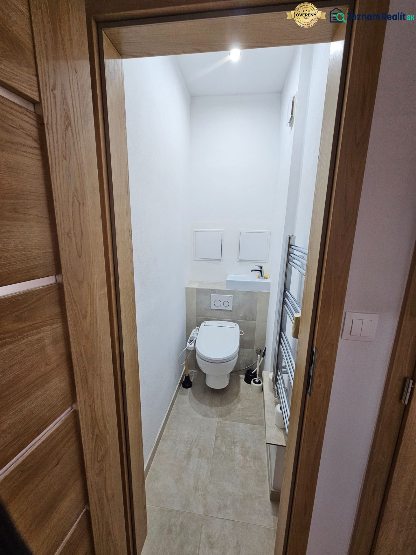 Compact toilet with ceramic tiles and a white sink in a 2-room apartment.