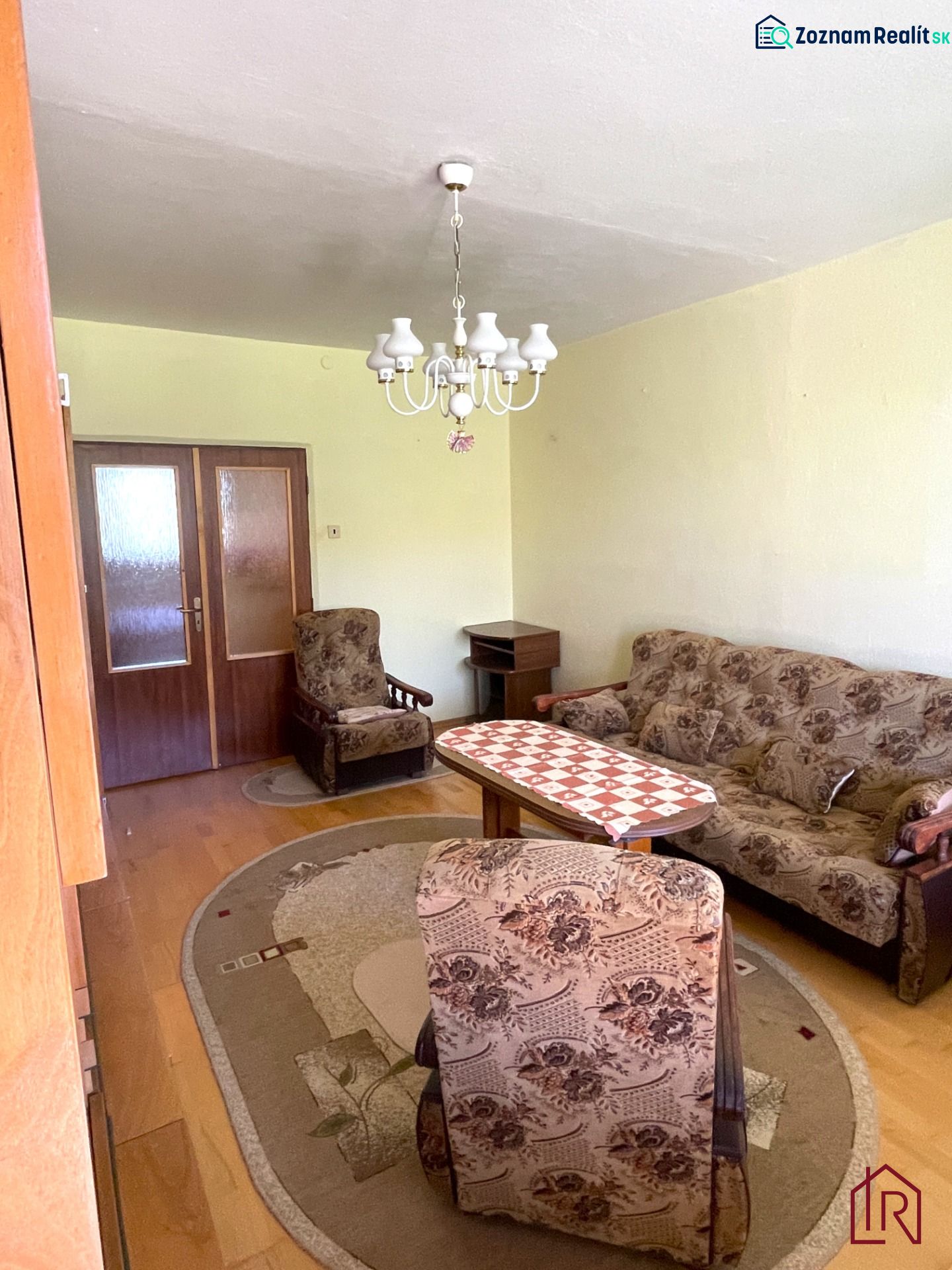 Living room in a two-room apartment with floral furniture and a wooden decor floor.