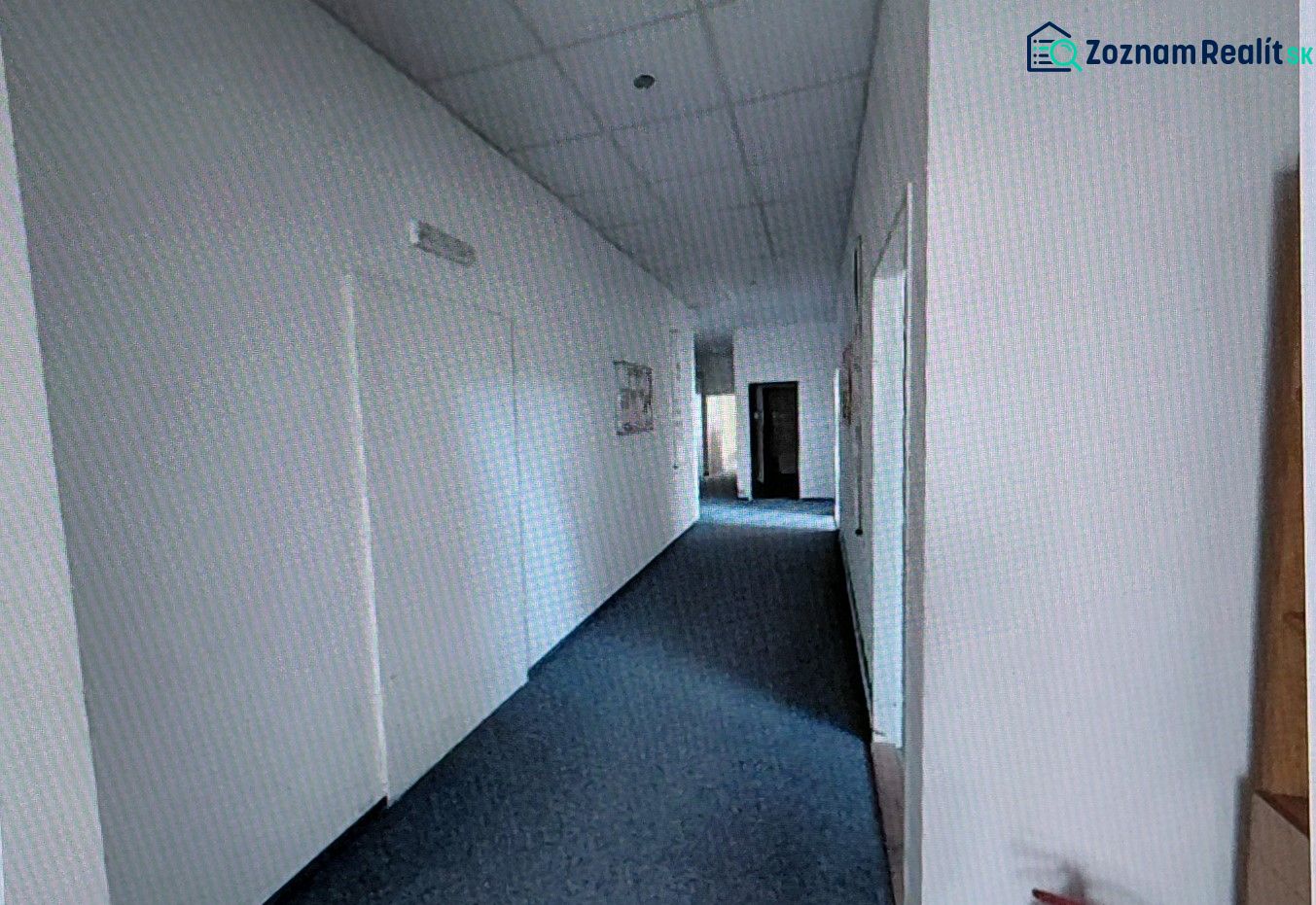 A narrow hallway with light walls and carpet in an office.