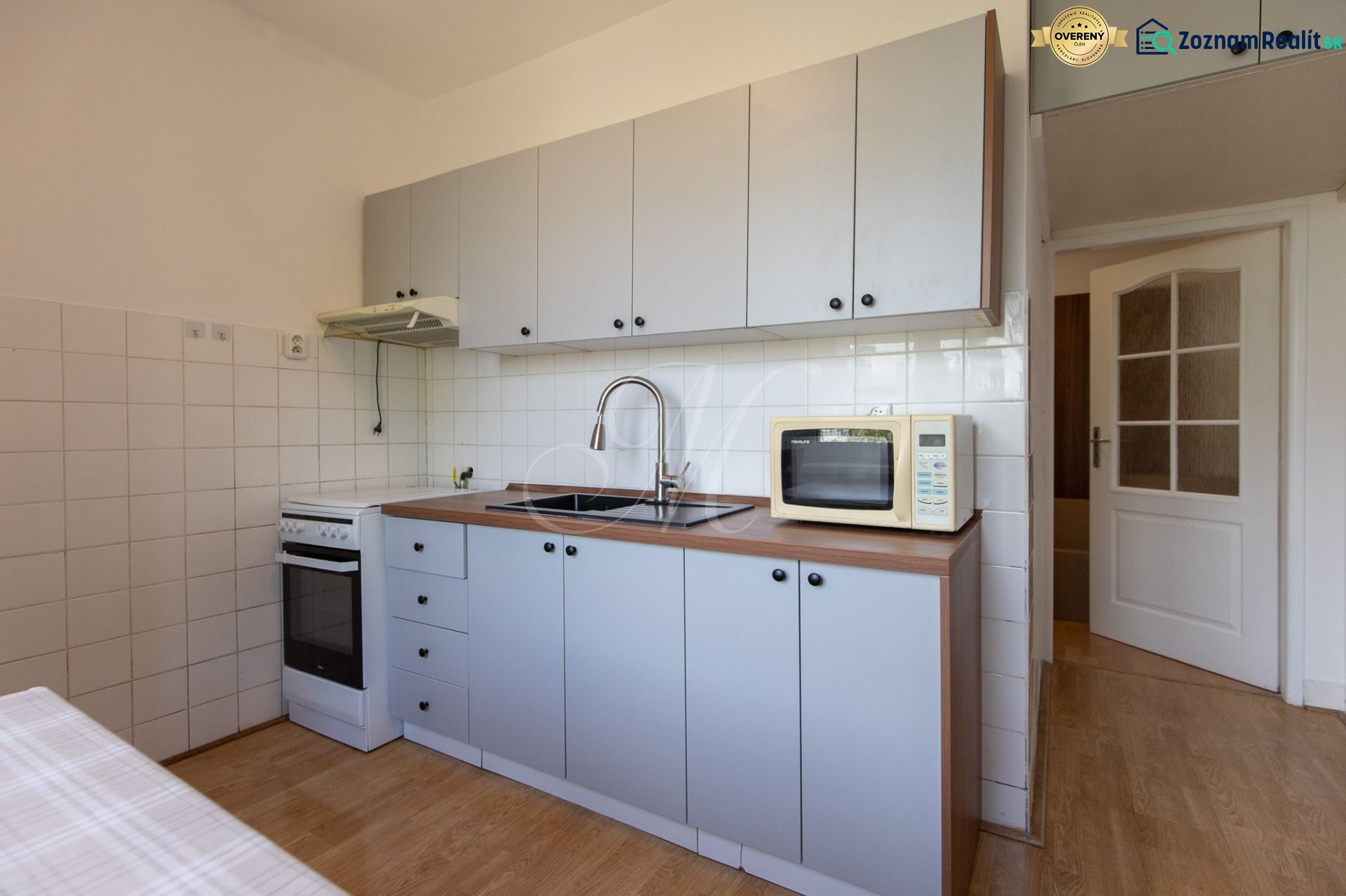 A kitchen in a 3-room apartment with a microwave, stove, and wooden decor flooring.