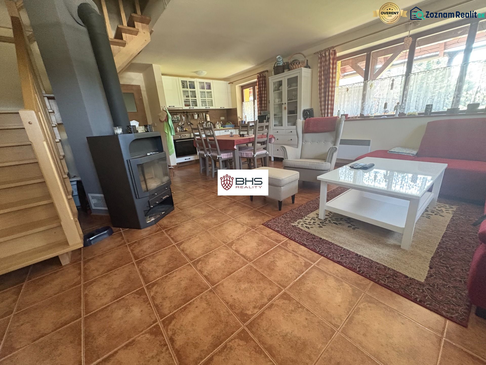 Interior of a cabin with a staircase, seating area, fireplace, kitchen, and wooden decor flooring.