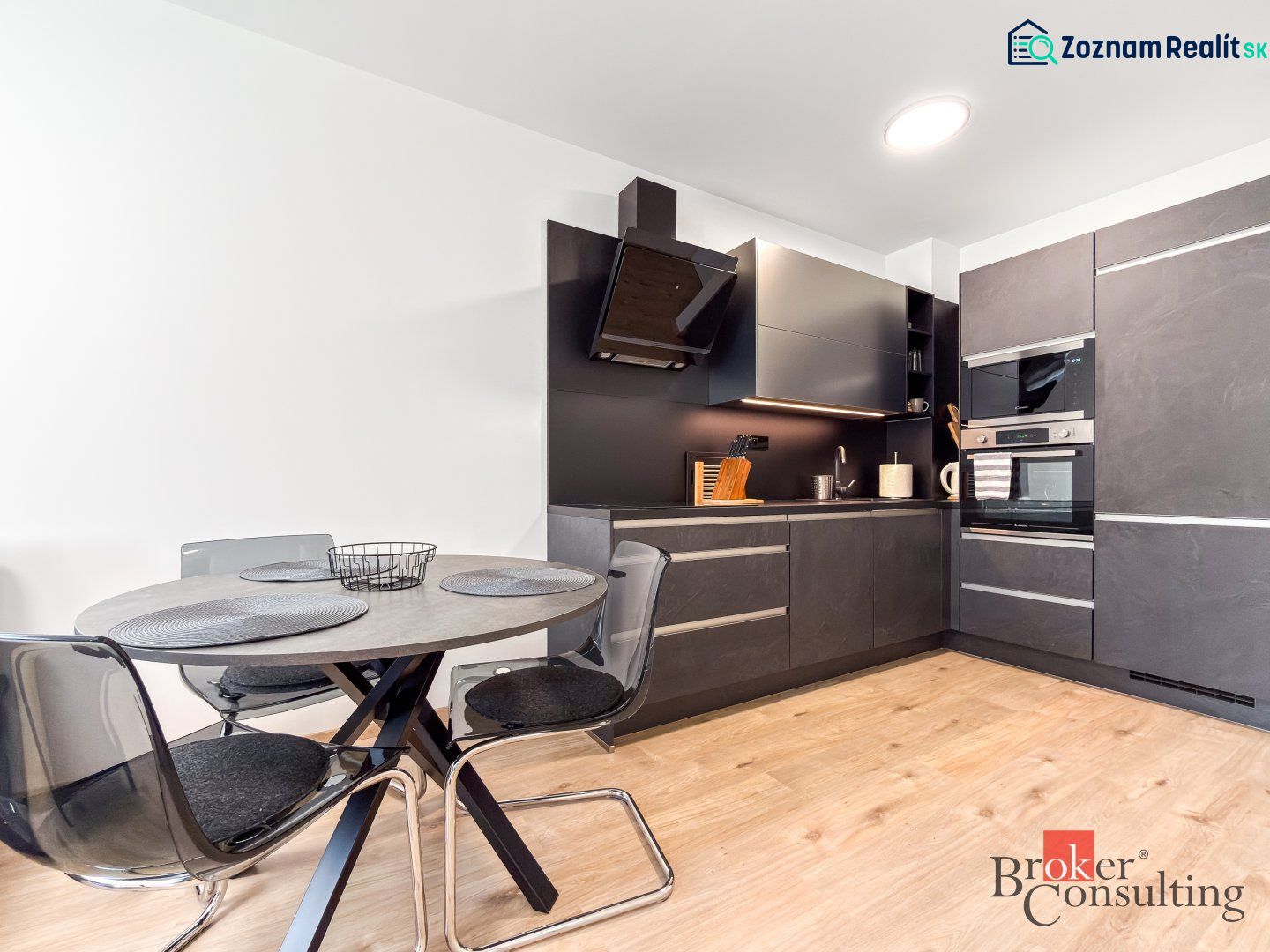 A kitchen in a studio apartment with dark cabinets and a wooden-patterned floor.