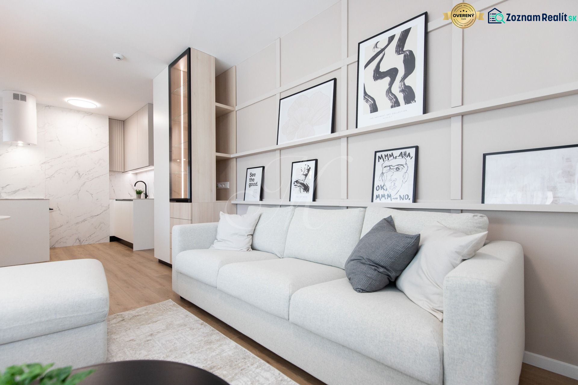Living room of a two-room apartment with wood-patterned flooring, a sofa, and modern art.